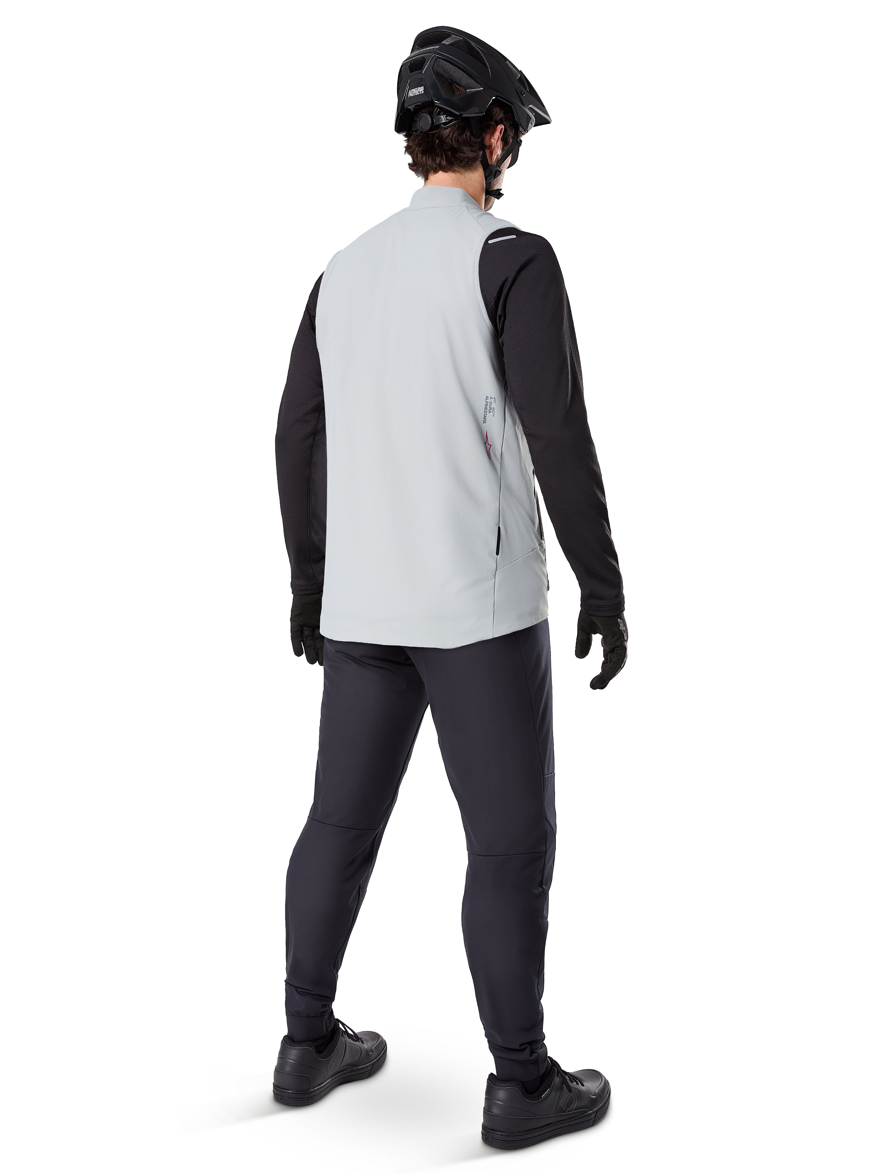 Alpinestars A-Dura Termisk Väst, Titanium Gray, ryggvy av modell som bär den isolerade cykelvästen över en svart långärmad tröja och mörka byxor, komplett med en svart mountainbikehjälm och handskar, designad för terrängkörning i kallt väder