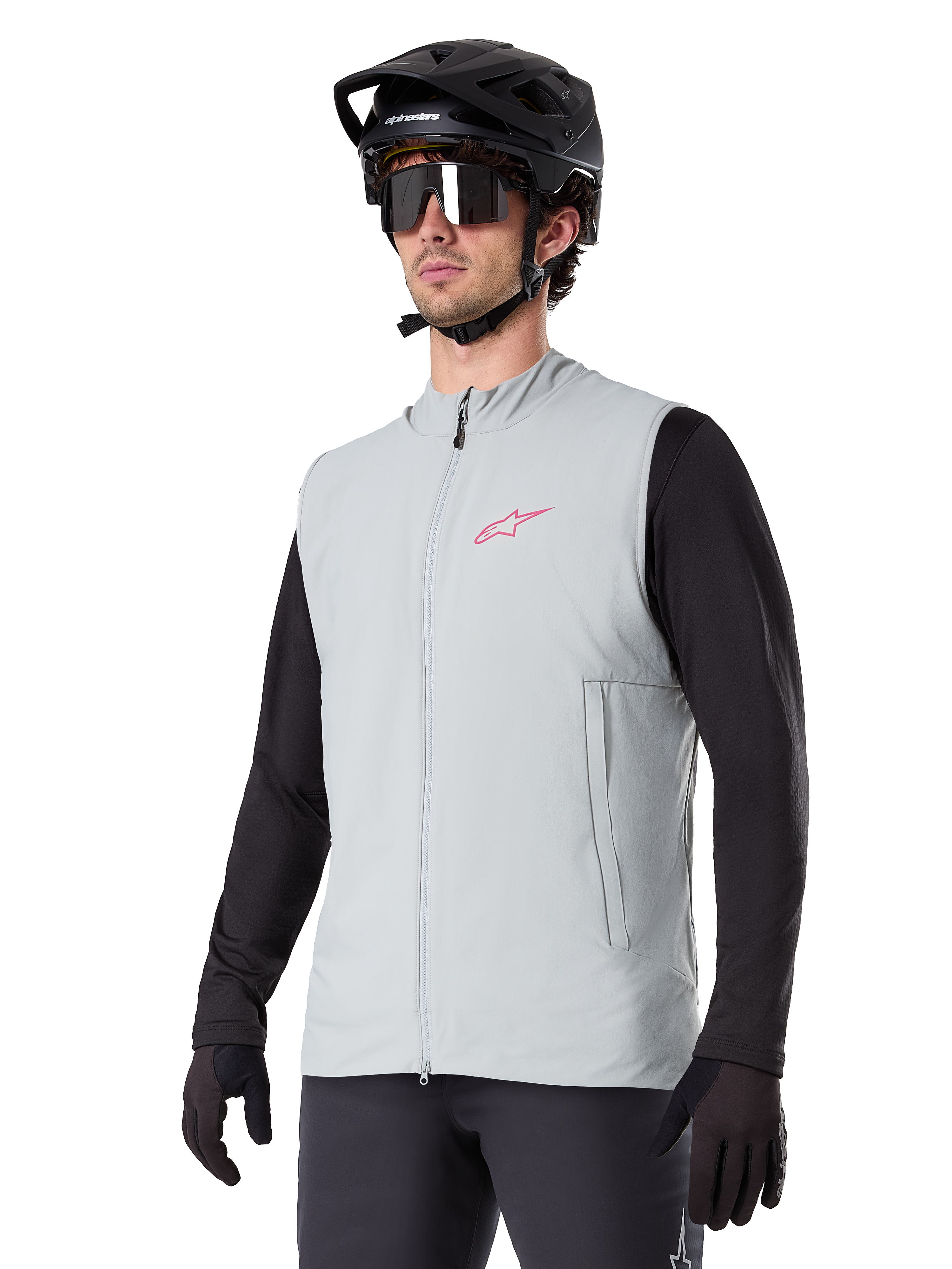 Alpinestars A-Dura Thermal Vest, titangrå, isolerad cykelväst, bärs över en svart långärmad tröja med en svart mountainbikehjälm och handskar, med en rosa logotyp på bröstet och vertikala sidofickor med dragkedja