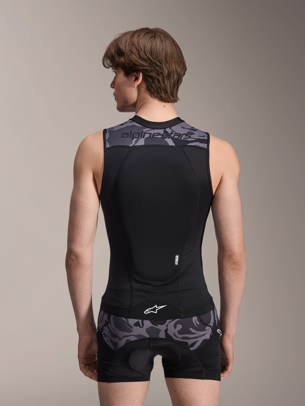 Alpinestars A-Motion Plasma skyddsväst, Black Camo, ryggvy på manlig modell, ventilerande meshkonstruktion med integrerat Nucleon Plasma-ryggskydd, grå kamouflagedetaljer på axlar och midja, Alpinestars-branding