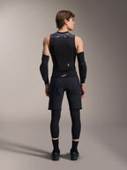 Alpinestars A-Motion Plasma skyddsväst, vy bakifrån, svart med grå kamouflagemönstrade axeldetaljer, bärs av modell med svarta armbågsskydd, cykelshorts över leggings och svarta cykelskor, visar det integrerade ryggskyddet