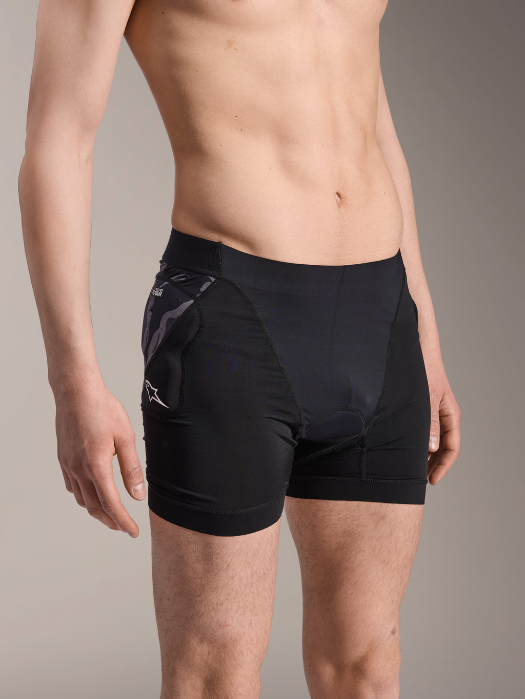 Alpinestars A-Motion Plasma skyddsboxershorts, svarta underställsshorts för cykling, kamouflagemönstrat höftskydd med vit Astar-logotyp, andningsbart meshtyg, skyddsutrustning för mountainbike