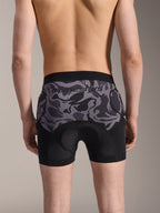Alpinestars A-Motion Plasma skyddsboxershorts, MTB-skyddsshorts, Black Camo, bakifrån buren av en modell, med Alpinestars-logotyp på en meshpanel i kamouflage, integrerad chamoisdyna och fickor för höftskydd, ventilerande baslager för terrängcykling