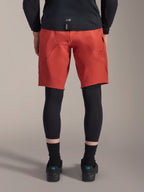 Alpinestars A-Motion Plasma knäskydd, svarta MTB-knäskydd, vy bakifrån burna under röda mountainbike-shorts med en svart cykeltröja och tekniska cykelskor, skyddsutrustning för mountainbikecykling