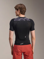 Alpinestars A-Motion Plasma skyddsjacka - kortärmad, svart med grå kamouflagedetaljer på övre ryggen, ryggvy som visar integrerat ryggskydd och vit Astars-logotyp i nederkanten, bärs med röda shorts, teknisk skyddsutrustning för mountainbike