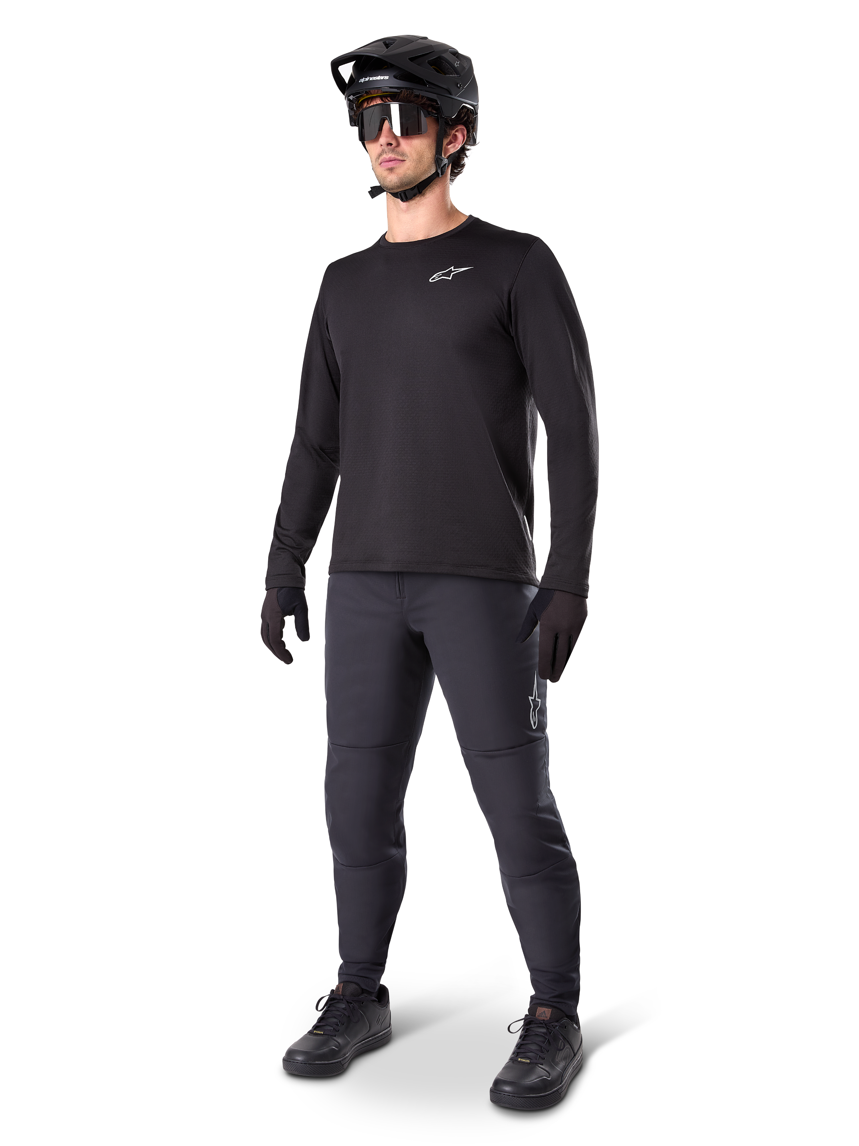 Mountainbike-cyklist iklädd Alpinestars A-Dura Thermal byxor, svarta, matchade med en svart långärmad tröja, svart hjälm och solglasögon, med en silverfärgad Alpinestars-logotyp på vänster lår, designade för terrängcykling i kallt väder