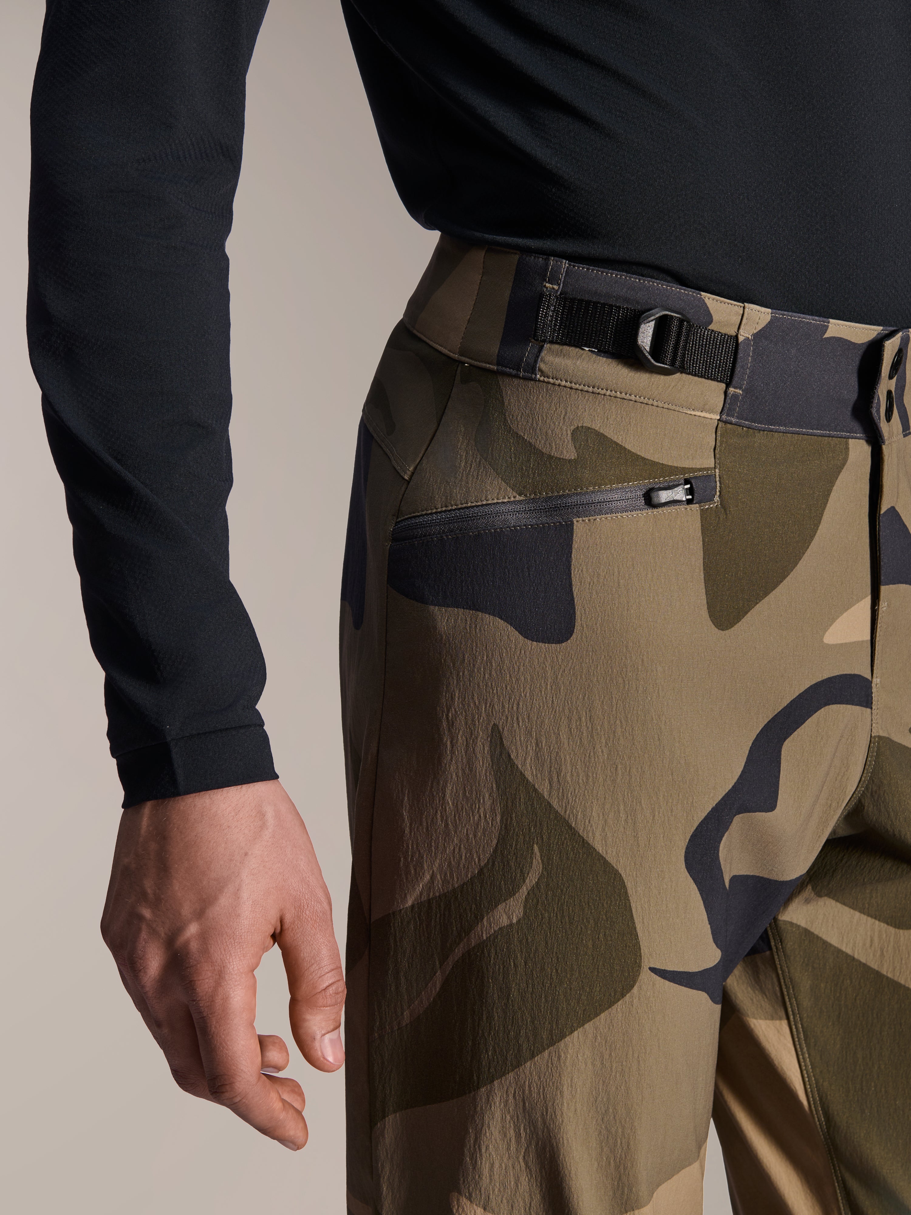 Alpinestars A-Dura Camo Pant, MTB-byxor, brunt kamouflage, närbild på den justerbara midjeremmen på sidan och blixtlåsförsedd nätfodrad ficka, slitstarkt 2-vägs stretchmaterial för mountainbike