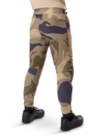 Alpinestars A-Dura Camo Pant, MTB-byxor, brunt kamouflagemönster med beige och mörkgrå detaljer, sedda bakifrån med svarta sneakers, avsmalnande ben och elastiska muddar, slitstarkt 2-vägs stretchmaterial för mountainbike