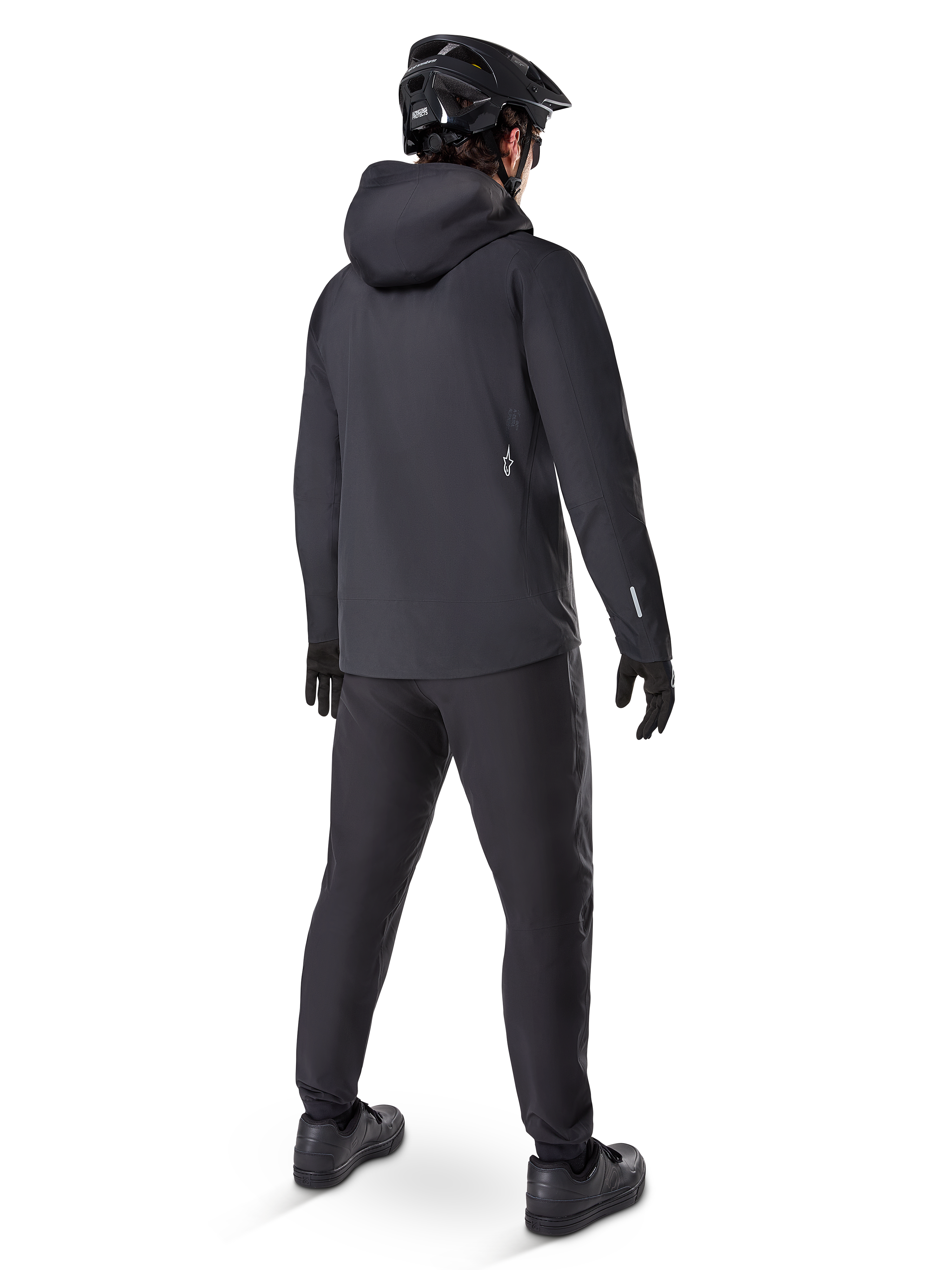 Alpinestars A-Dura Waterproof Pants, MTB-byxor, svarta, sedda bakifrån på en cyklist klädd i en helsvart mountainbike-utrustning inklusive huvjacka och hjälm, slitstark vattentät utrustning för leriga stigar