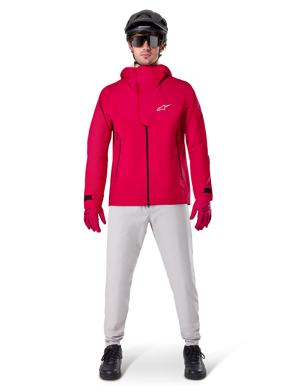 Alpinestars A-Dura Waterproof Pants, MTB-byxor, Titanium Gray, bärs med en starkröd jacka med huva, röda handskar och en svart mountainbikehjälm, professionell vattentät cykelutrustning för våta terrängförhållanden
