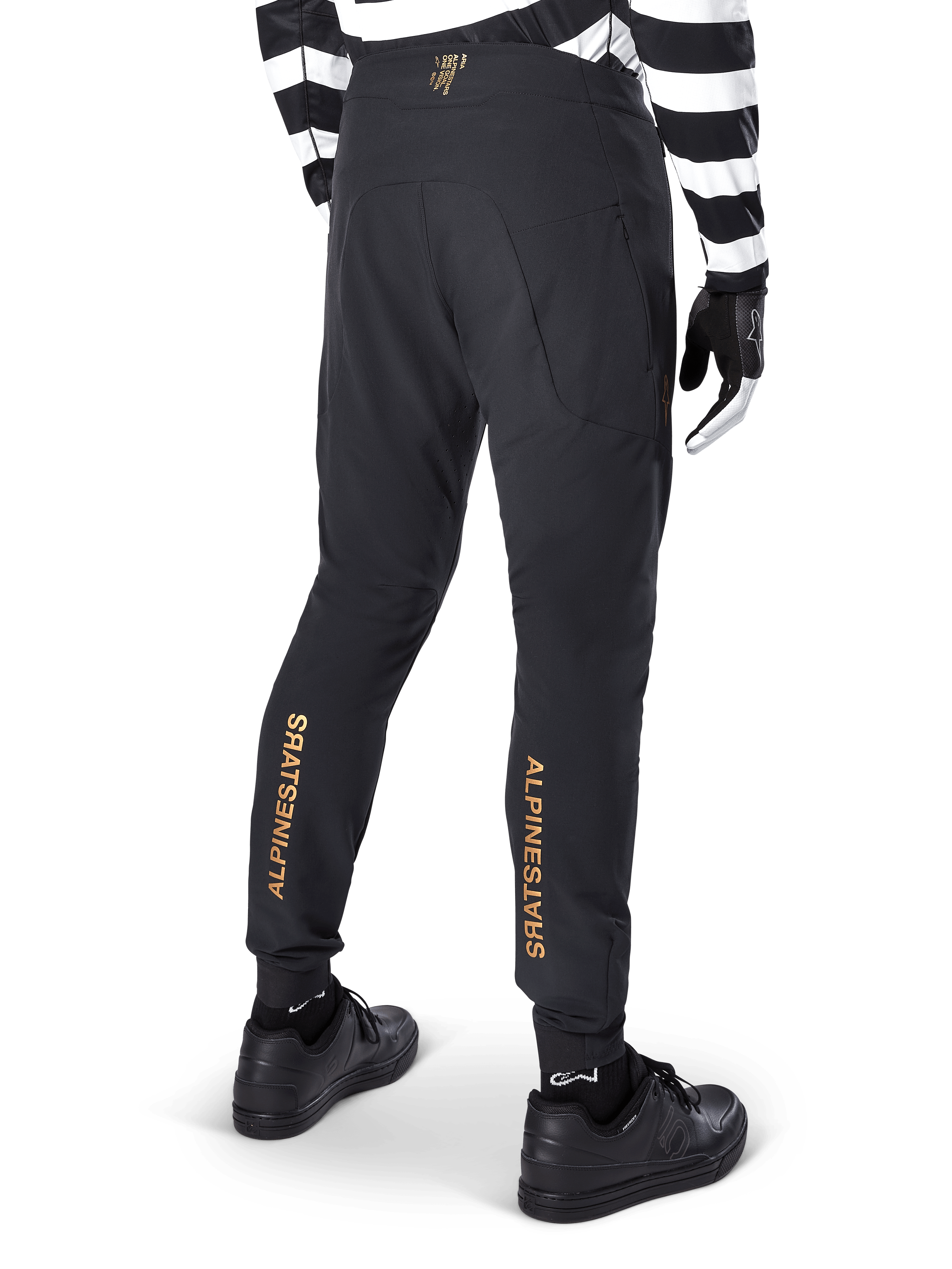 Alpinestars A-Aria Elite Pants, Black MTB Pants, rear view, featuring vertical gold Alpinestars branding on the back of the legs, worn with a black and white striped jersey and black shoes, performance cycling apparel for mountain biking