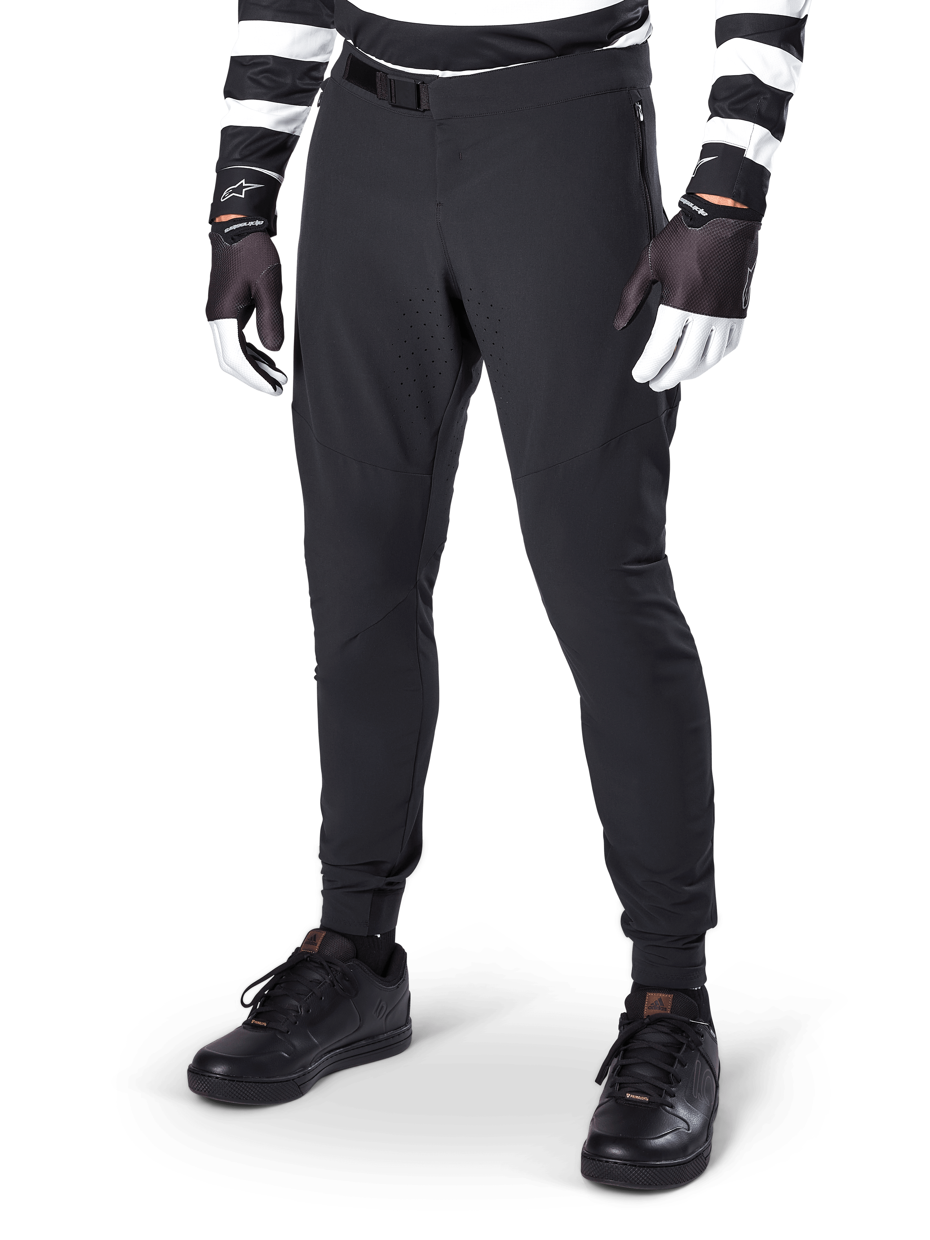 Alpinestars A-Aria Elite-byxor, svarta mountainbike-byxor med laserskuren ventilation på låren och magnetiskt spänne, bärs med svart- och vitrandig tröja och handskar, högpresterande MTB-utrustning för terrängcykling