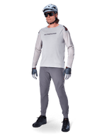 Alpinestars A-Aria Elite byxor, mörkgrå MTB-byxor, burna av en cyklist med en ljusgrå långärmad tröja och grå hjälm, med laserskuren ventilation på låren och en avsmalnande prestandapassform för mountainbikecykling.