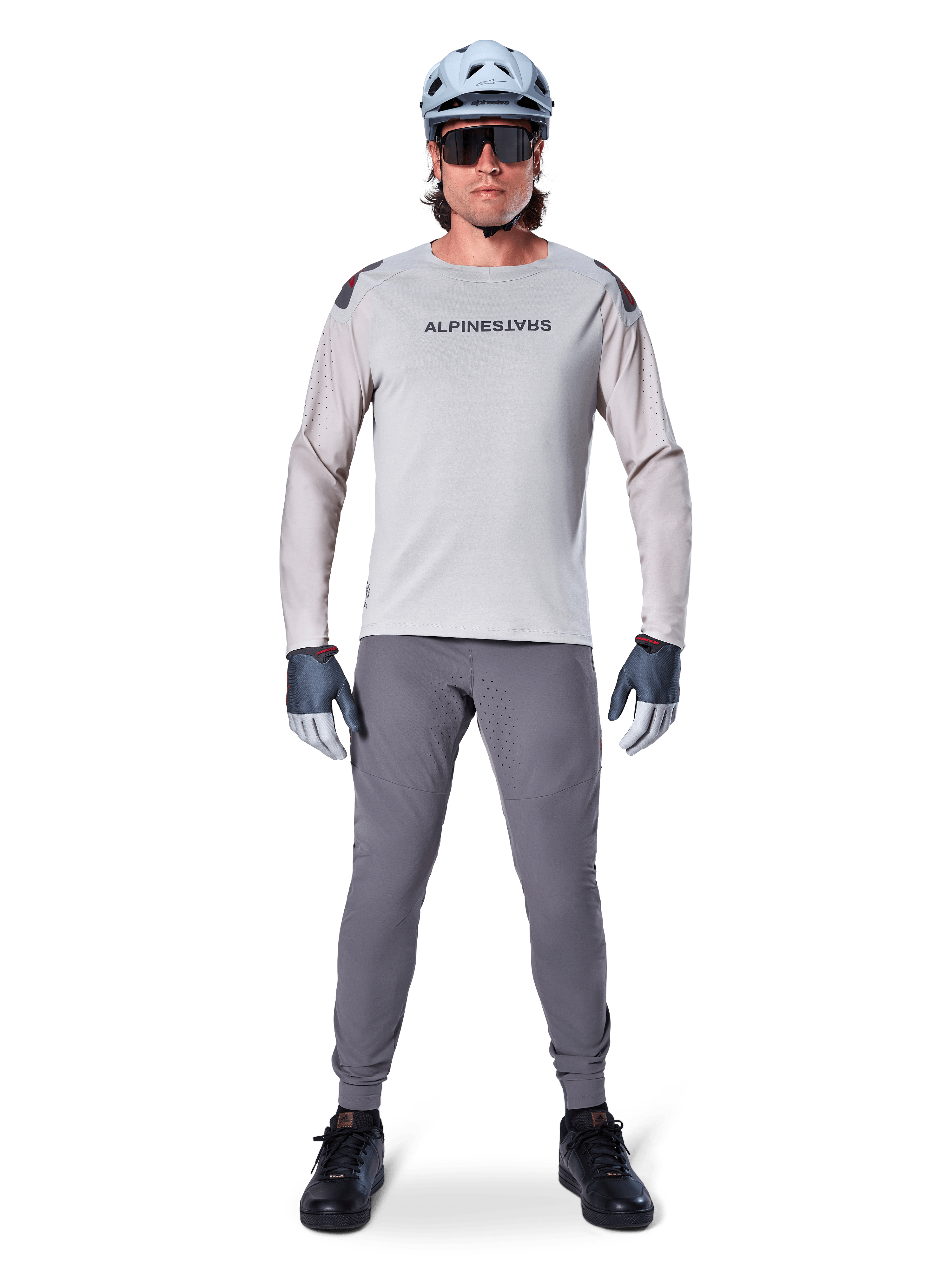 Alpinestars A-Aria Elite byxor, mörkgrå mountainbike-byxor, bärs av en cyklist i en ljusgrå långärmad tröja, ljusblå hjälm och svarta skor, med synliga laserperforeringar på innerbenen och en slimmad prestandapassform.