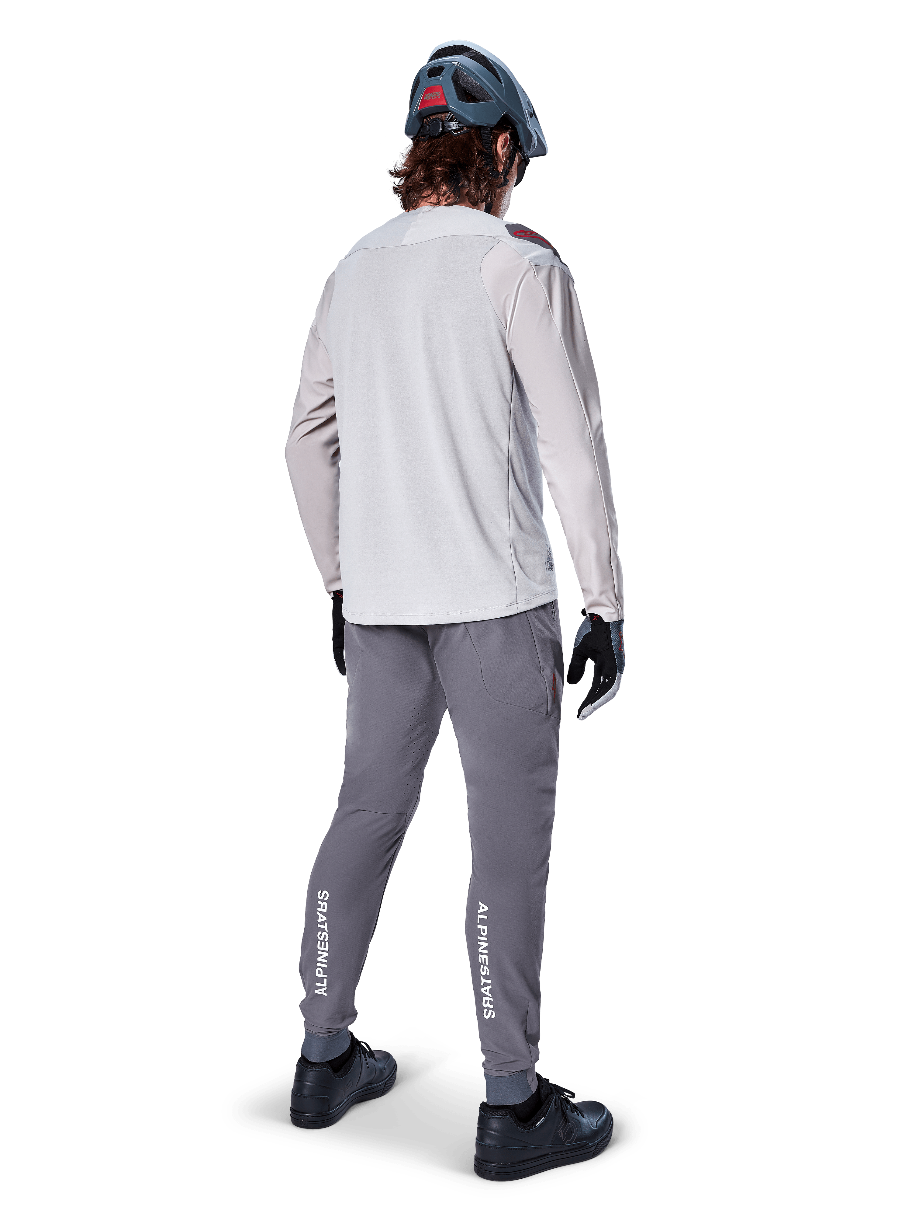 Alpinestars A-Aria Elite-byxor, MTB-byxor, mörkgrå, vy bakifrån av en cyklist i en hel outfit, vit Alpinestars-logotyp på underbenen, prestandapassform med laserperforeringar, matchad med en ljusgrå långärmad tröja och grå MTB-hjälm