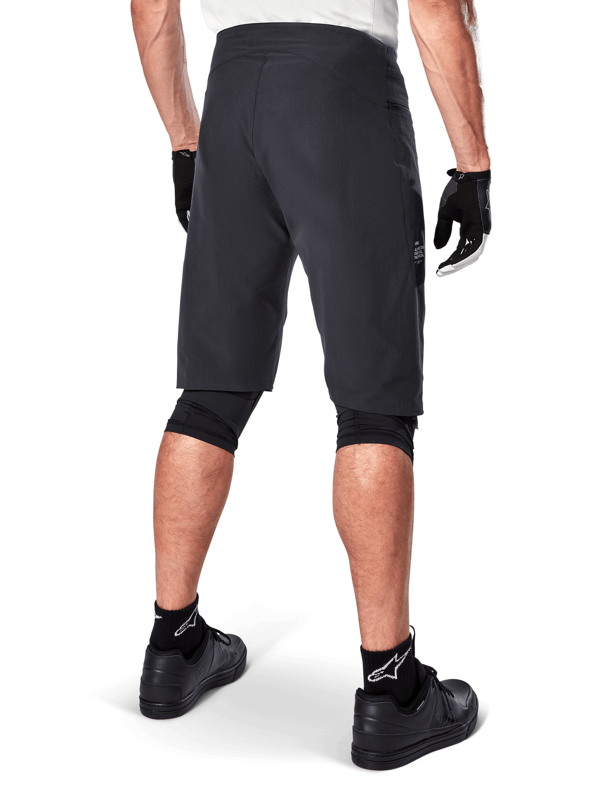 Alpinestars A-Aria Shorts, mountainbikeshorts, svarta, baksida som visar prestandapassform och stilren design, bärs med svarta handskar och strumpor med vit Astars-logotyp, teknisk cykelutrustning för terrängkörning