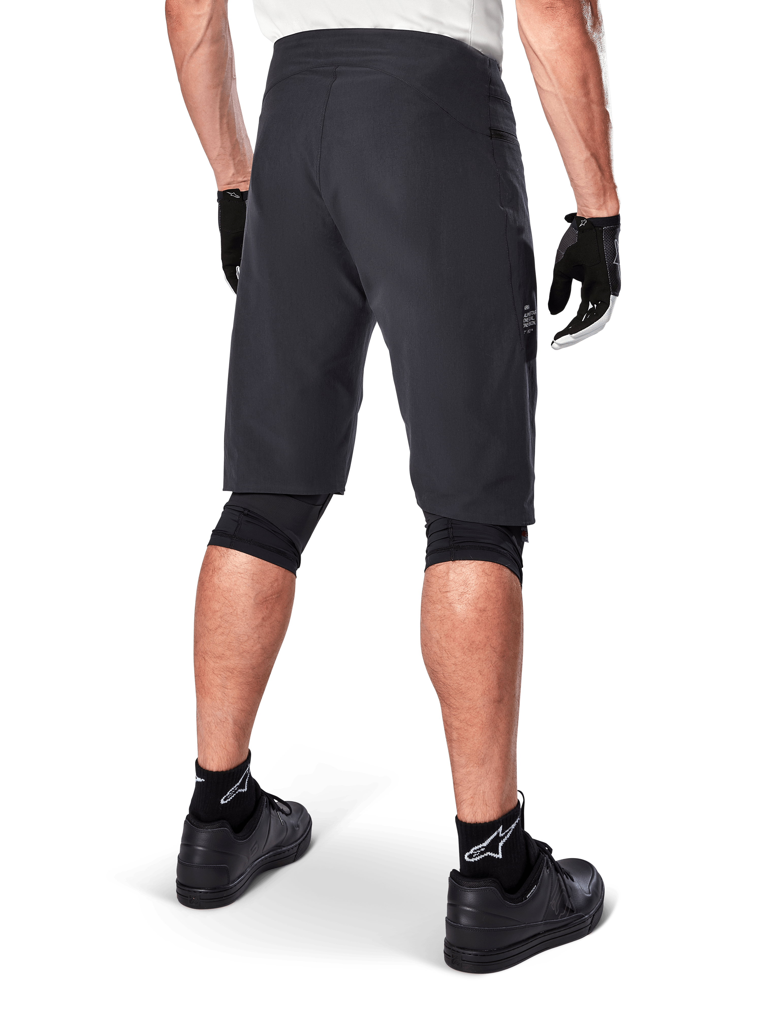Alpinestars A-Aria Shorts, mountainbikeshorts, svarta, baksida som visar prestandapassform och stilren design, bärs med svarta handskar och strumpor med vit Astars-logotyp, teknisk cykelutrustning för terrängkörning