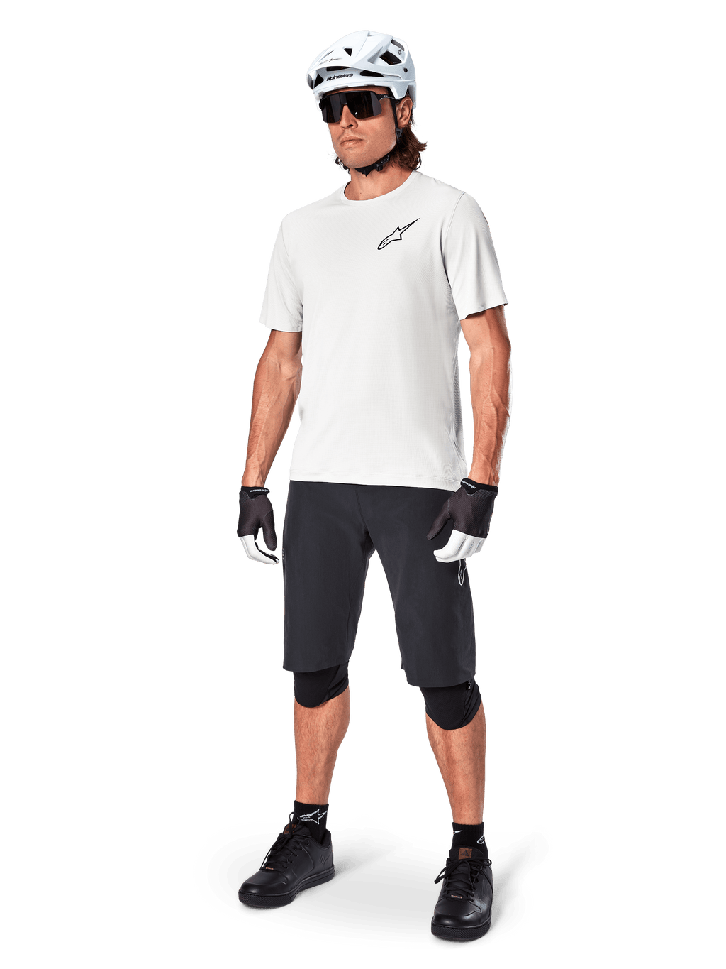 Manlig mountainbikecyklist iklädd Alpinestars A-Aria Shorts, svarta cykelshorts, matchat med en vit kortärmad tröja, vit mountainbikehjälm och svart funktionsutrustning, komplett outfit för terrängcykling