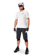 Manlig mountainbikecyklist iklädd Alpinestars A-Aria Shorts, svarta cykelshorts, matchat med en vit kortärmad tröja, vit mountainbikehjälm och svart funktionsutrustning, komplett outfit för terrängcykling