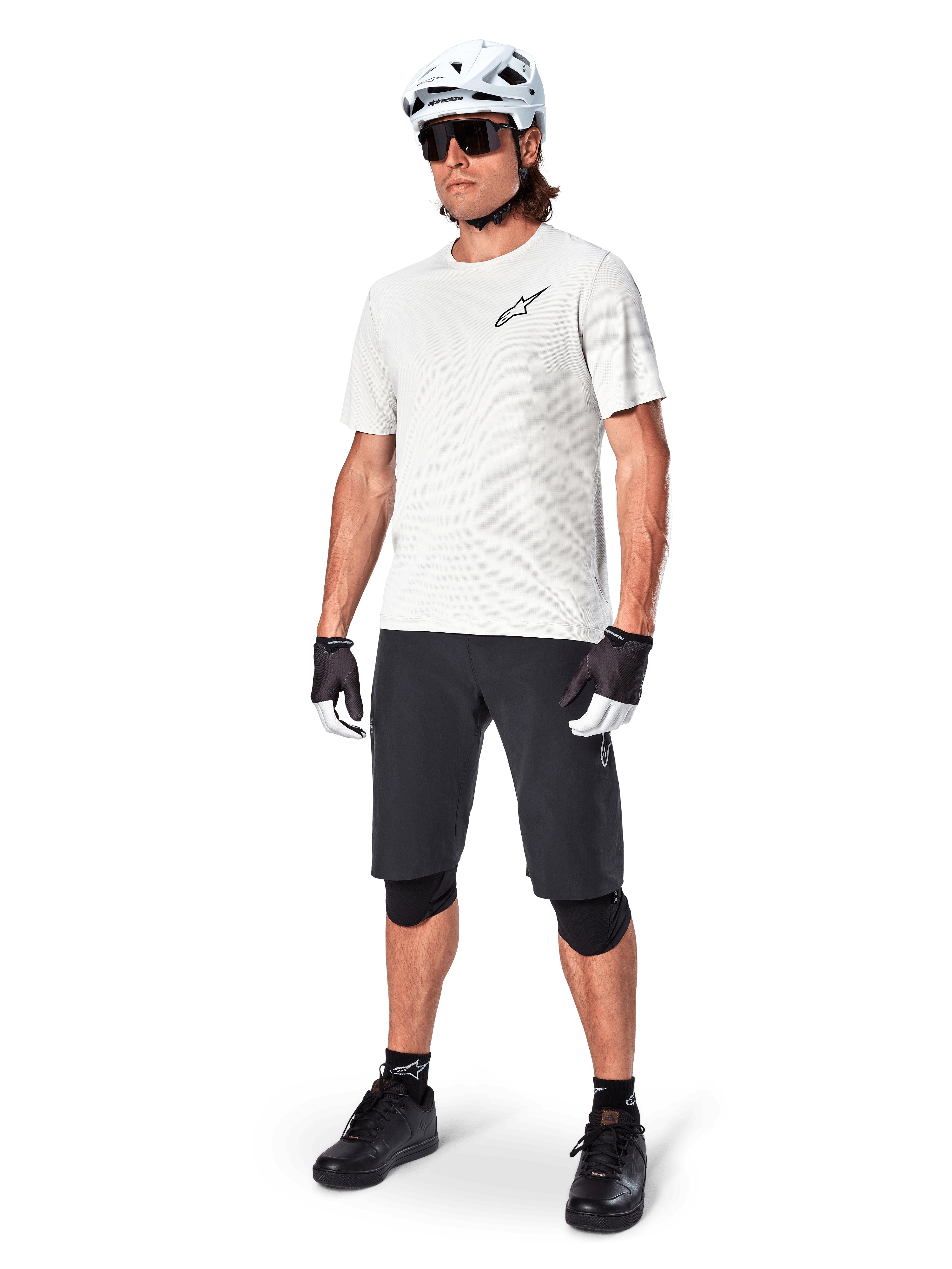 Manlig mountainbikecyklist iklädd Alpinestars A-Aria Shorts, svarta cykelshorts, matchat med en vit kortärmad tröja, vit mountainbikehjälm och svart funktionsutrustning, komplett outfit för terrängcykling