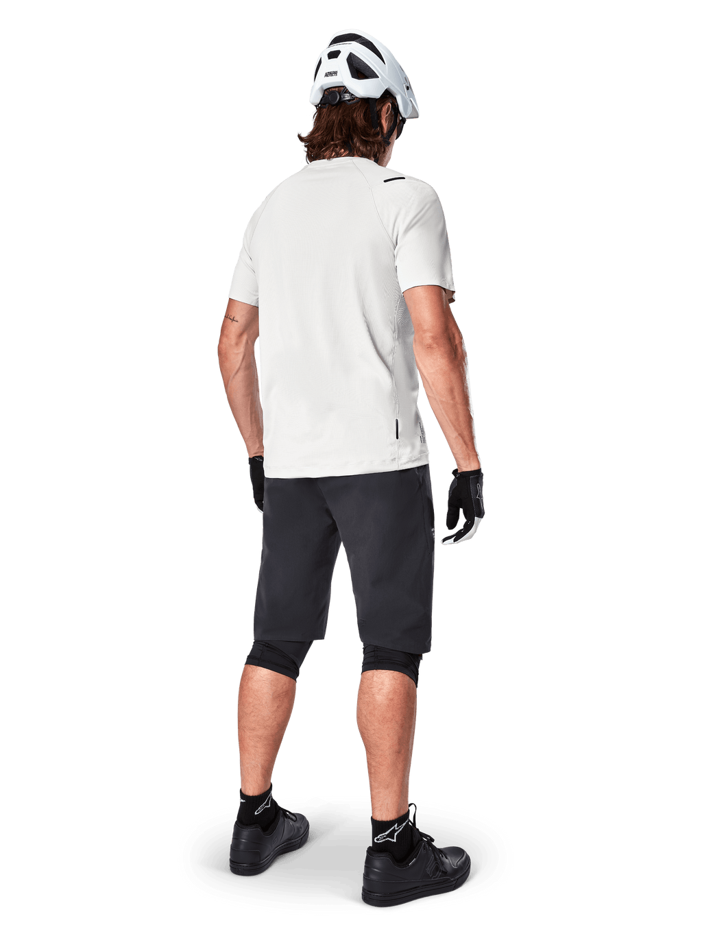 Mountainbikecyklist bakifrån bärande Alpinestars A-Aria Shorts i svart, vit kortärmad funktionströja, vit hjälm, svarta handskar och svarta mountainbikeskor, cykelutrustning för stigcykling