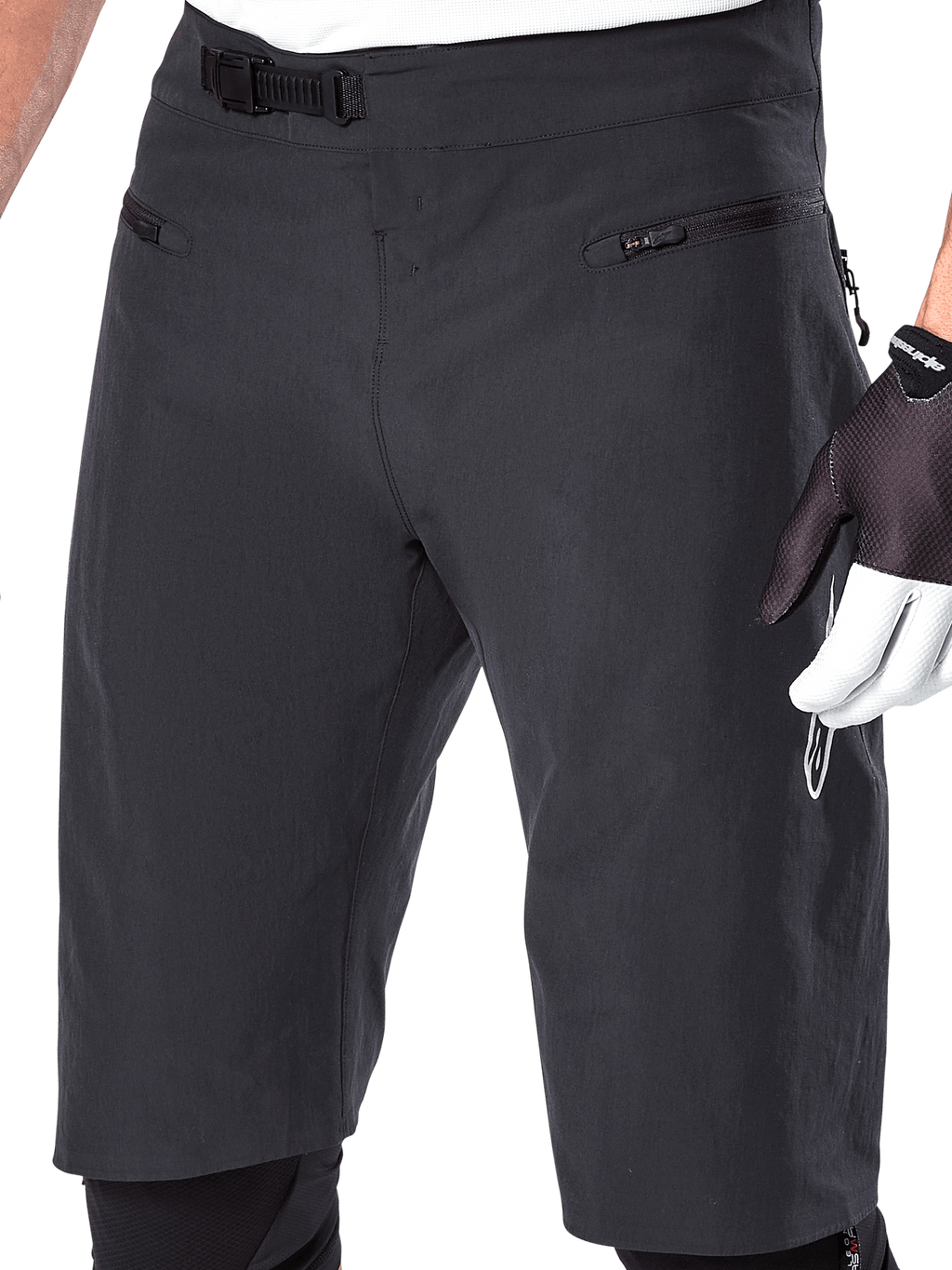 Alpinestars A-Aria Shorts, mountainbike-shorts, svarta, närbild på främre midja och lår som visar spärrspännet och fickor med dragkedja, bärs med svarta och vita cykelhandskar, prestandautrustning för stigcykling.