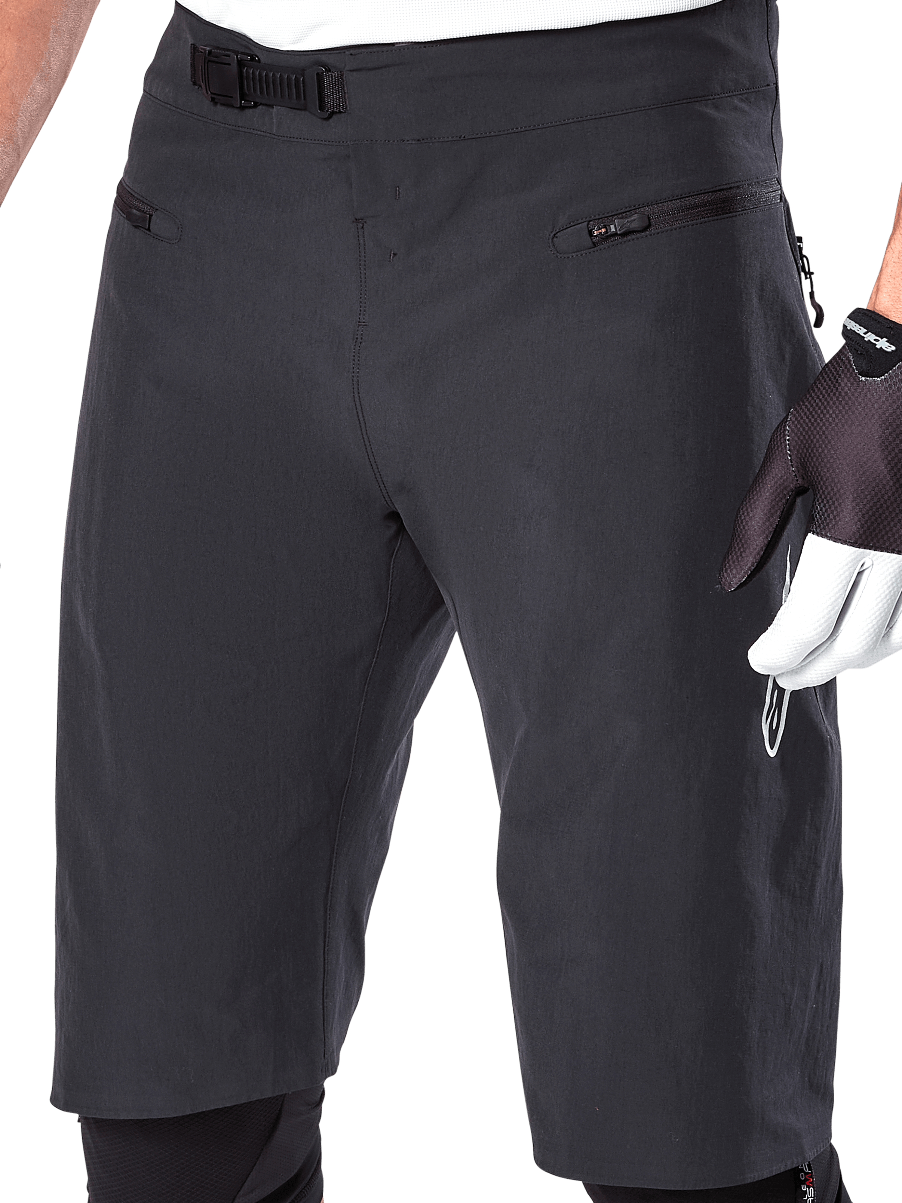 Alpinestars A-Aria Shorts, mountainbike-shorts, svarta, närbild på främre midja och lår som visar spärrspännet och fickor med dragkedja, bärs med svarta och vita cykelhandskar, prestandautrustning för stigcykling.