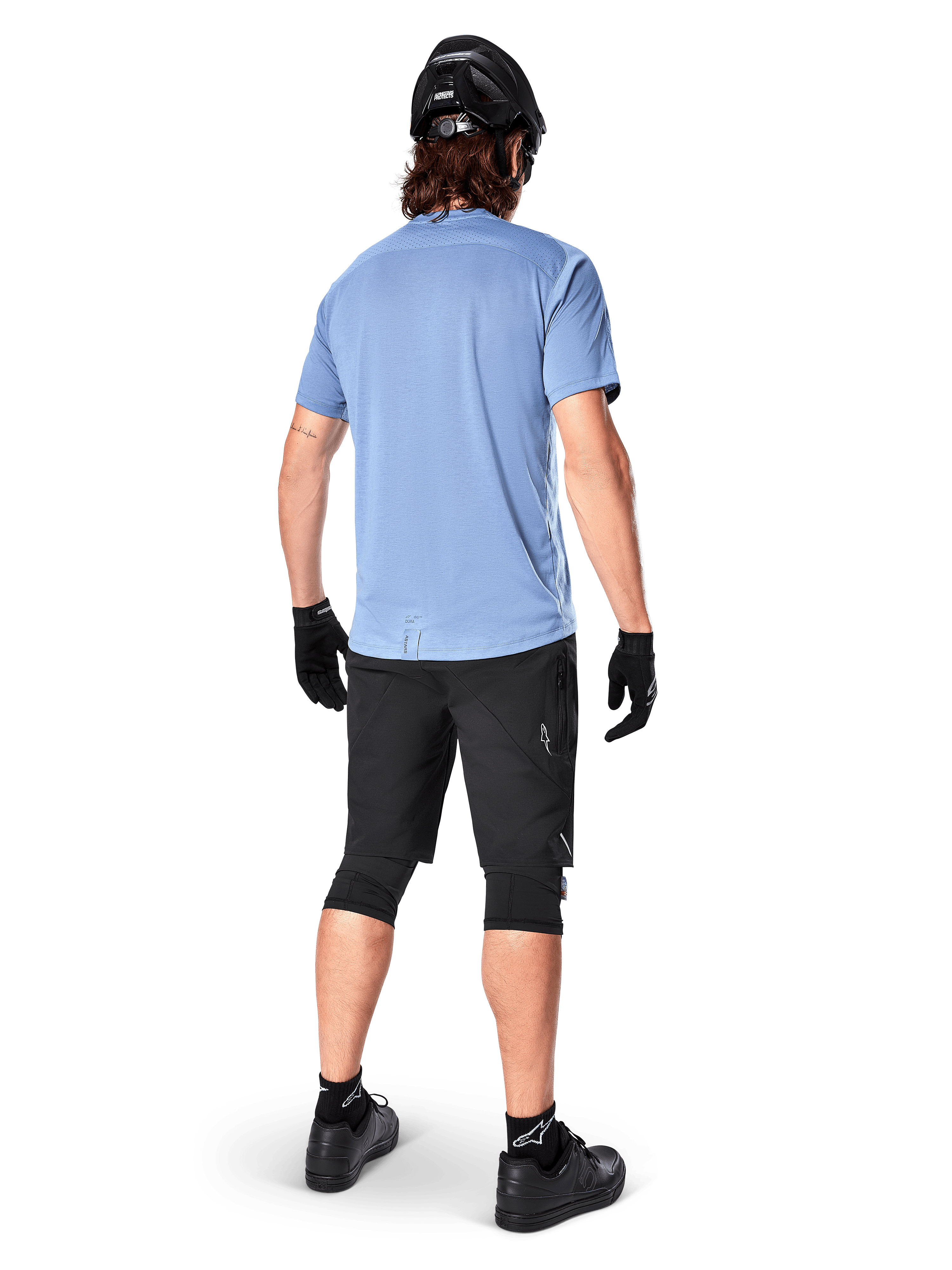Alpinestars A-Dura Elite Shorts, Mountain Bike Shorts, Black, rear view on model, worn with light blue short-sleeve shirt and black protective gear, technical design with zippered pockets and reflective details for off-road cycling