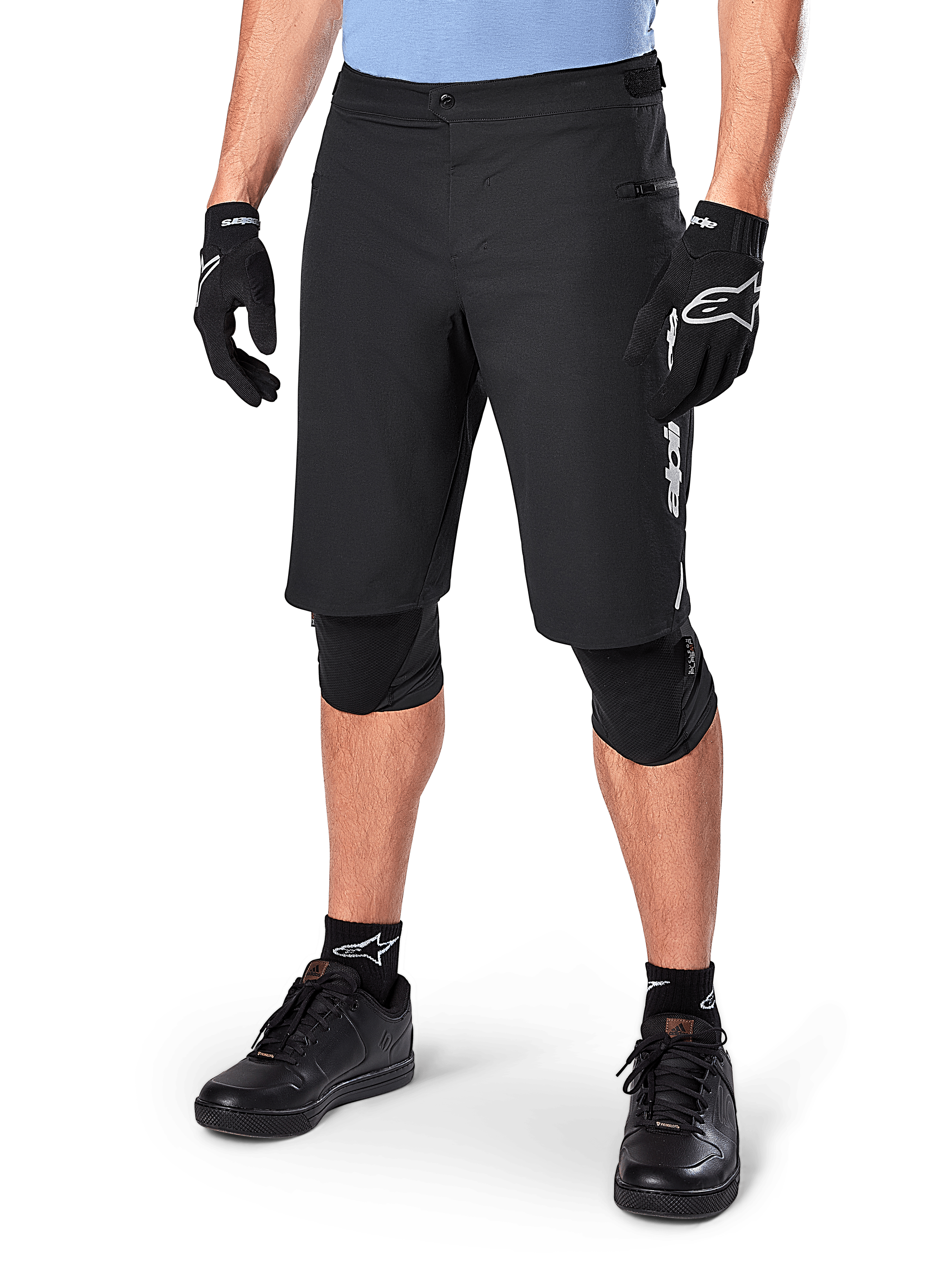 Alpinestars A-Dura Elite Shorts, Black MTB Mountain Biking Shorts, worn with light blue shirt and black knee protection, featuring a secure snap closure and zippered pocket, paired with black cycling shoes and gloves for a complete off-road outfit.