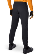 Alpinestars A-Dura-byxor, svarta MTB-byxor, sedda bakifrån, bärs med en orange långärmad tröja och svarta handskar, med elastiska muddar och slitstarkt textilmaterial för mountainbike