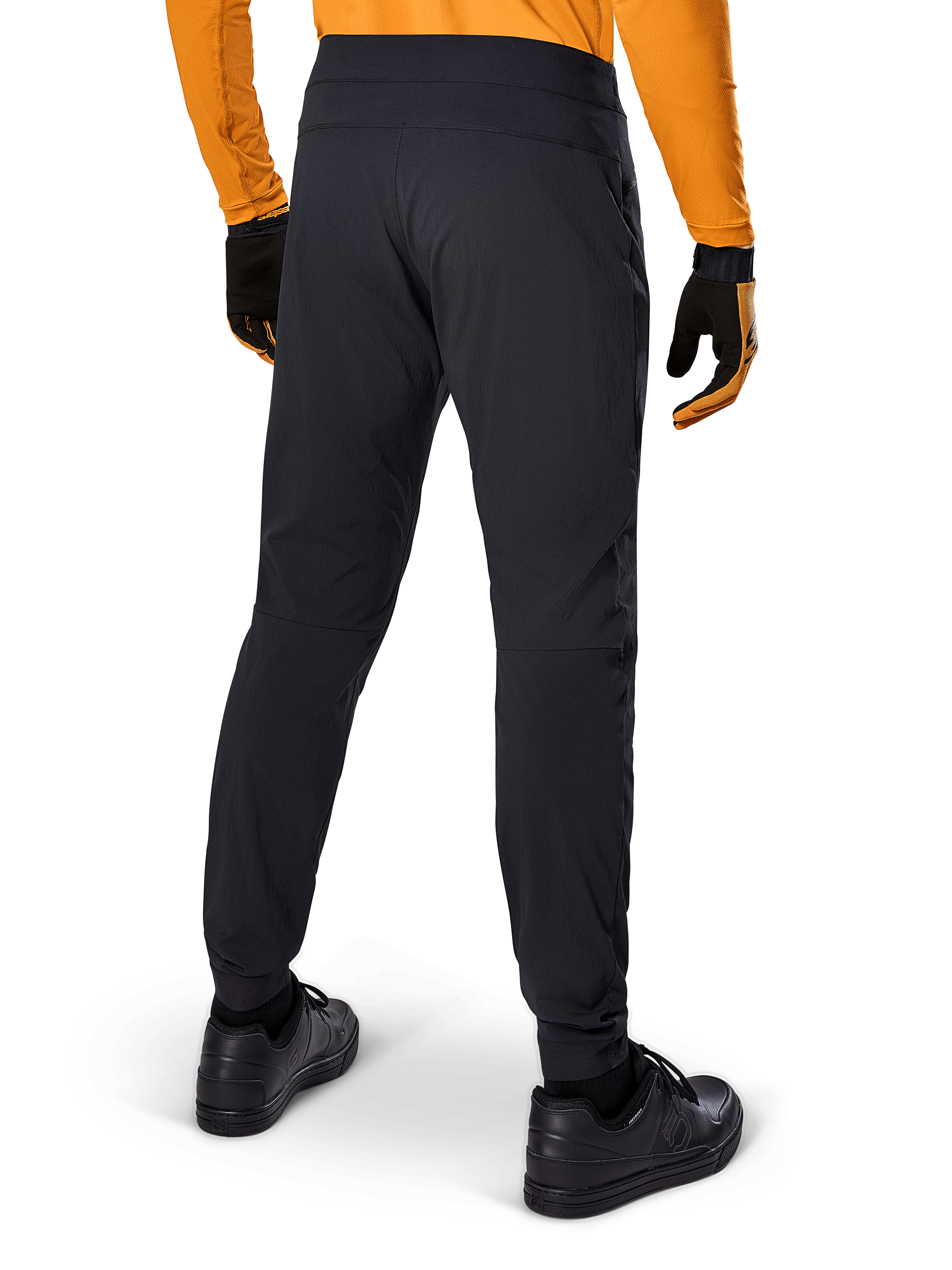 Alpinestars A-Dura-byxor, svarta MTB-byxor, sedda bakifrån, bärs med en orange långärmad tröja och svarta handskar, med elastiska muddar och slitstarkt textilmaterial för mountainbike