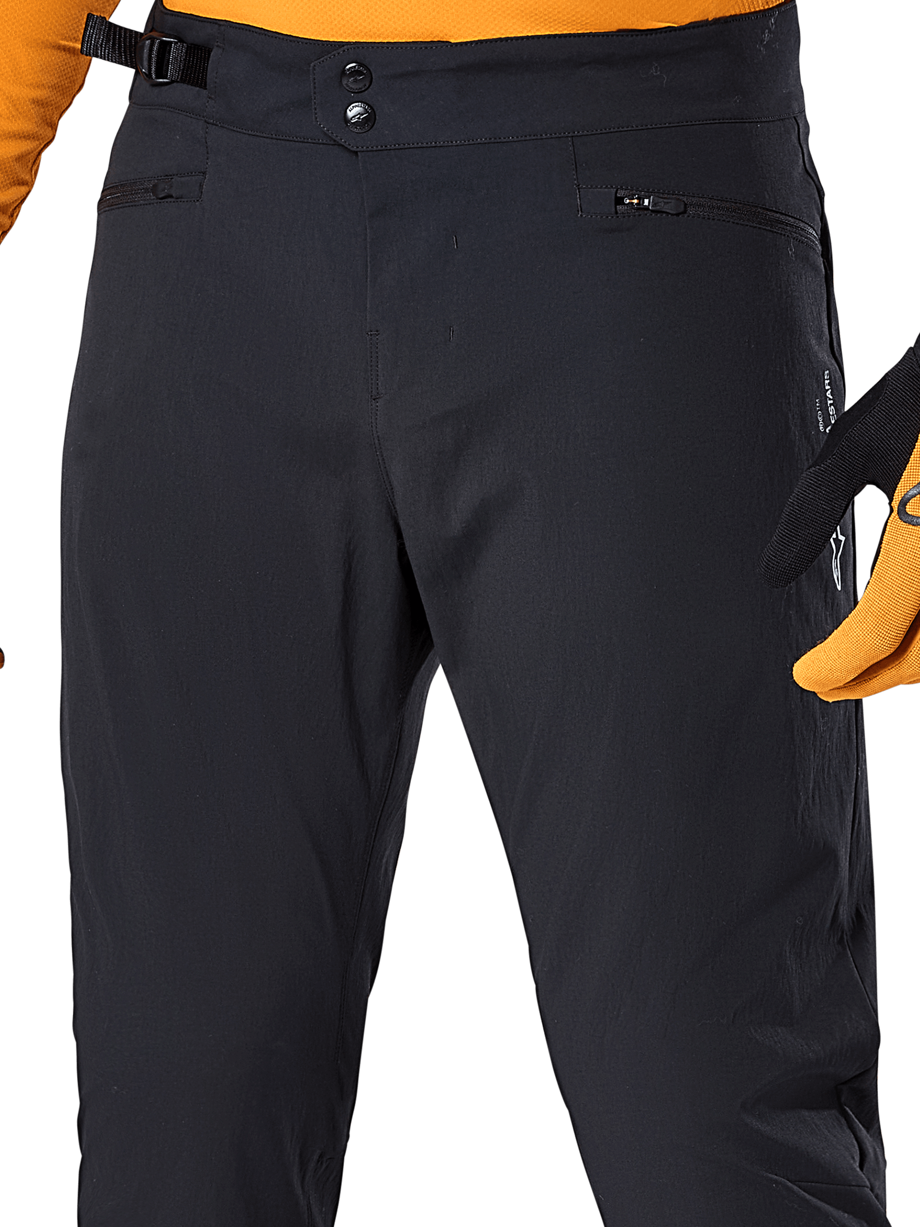 Alpinestars A-Dura Pants, svarta MTB-cykelbyxor, närbild med dubbel tryckknappsstängning i midjan, justerbar sidostängning och blixtlåsförsedda fickor, matchade med en orange tröja och handskar