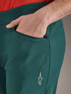 Alpinestars A-Dura byxor i färgen Dark Pine, närbild på blixtlåsförsedd ficka med hand, med vit Alpinestars-logotyp och text på låret, slitstarka MTB-cykelbyxor