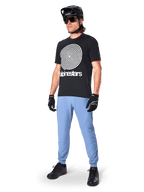 Alpinestars A-Dura byxor, MTB-byxor, Infinity Blue, bärs med svart grafisk t-shirt med vit spirallogotyp, svart hjälm, solglasögon och svarta handskar, professionell mountainbikeutrustning