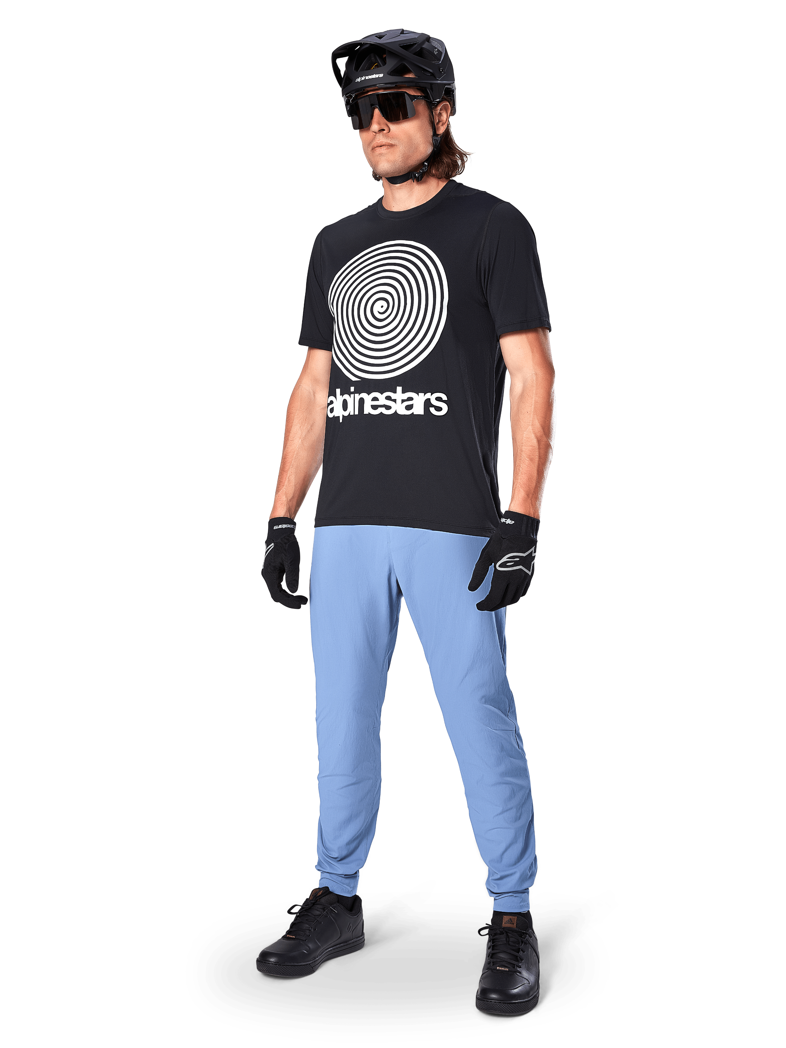 Alpinestars A-Dura byxor, MTB-byxor, Infinity Blue, bärs med svart grafisk t-shirt med vit spirallogotyp, svart hjälm, solglasögon och svarta handskar, professionell mountainbikeutrustning