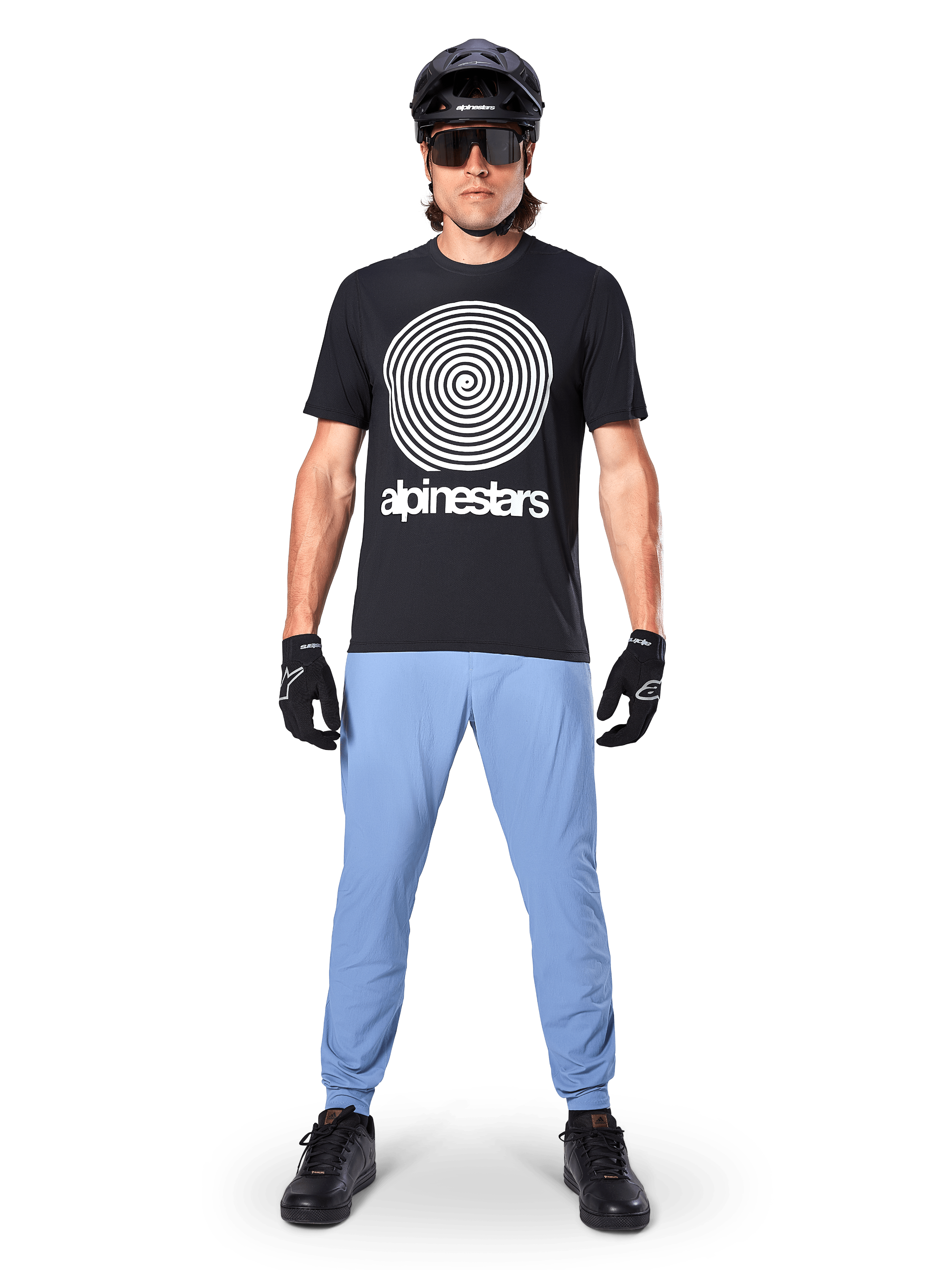 Alpinestars A-Dura byxor, Infinity Blue, MTB-byxor som bärs med en svart t-shirt med spiralgrafik, svarta handskar och en svart hjälm, med ett slitstarkt stretchmaterial och elastiska muddar, prestandautrustning för mountainbike