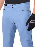 Alpinestars A-Dura-byxor, MTB-byxor, Infinity Blue, närbild på midjan med dubbel tryckknappsstängning och sidjustering, blixtlåsförsedda fickor, bärs med svarta Alpinestars-handskar