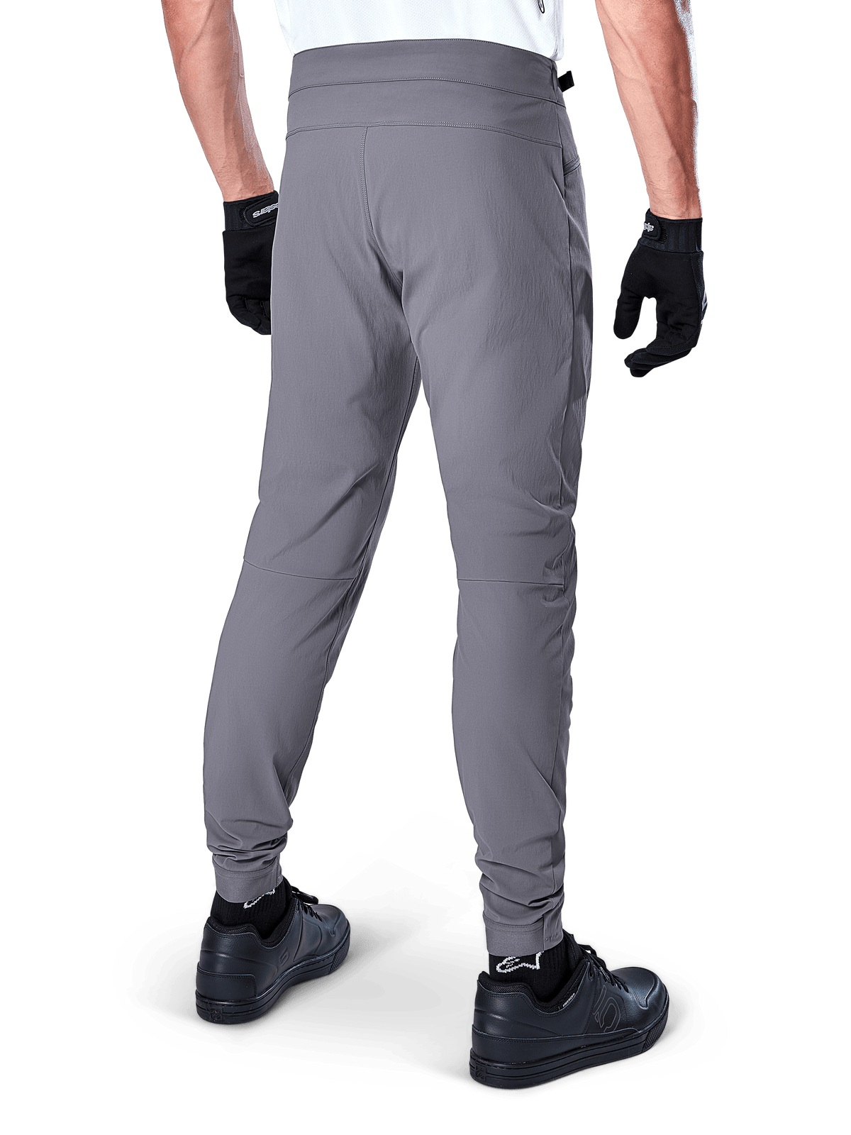 Alpinestars A-Dura Pants, MTB-byxor, mörkgrå, bakvy av modell som bär utrustningen, med ett slitstarkt 2-vägs stretchtyg och elastiska muddar, matchat med svarta handskar och sneakers för en cykelklar look