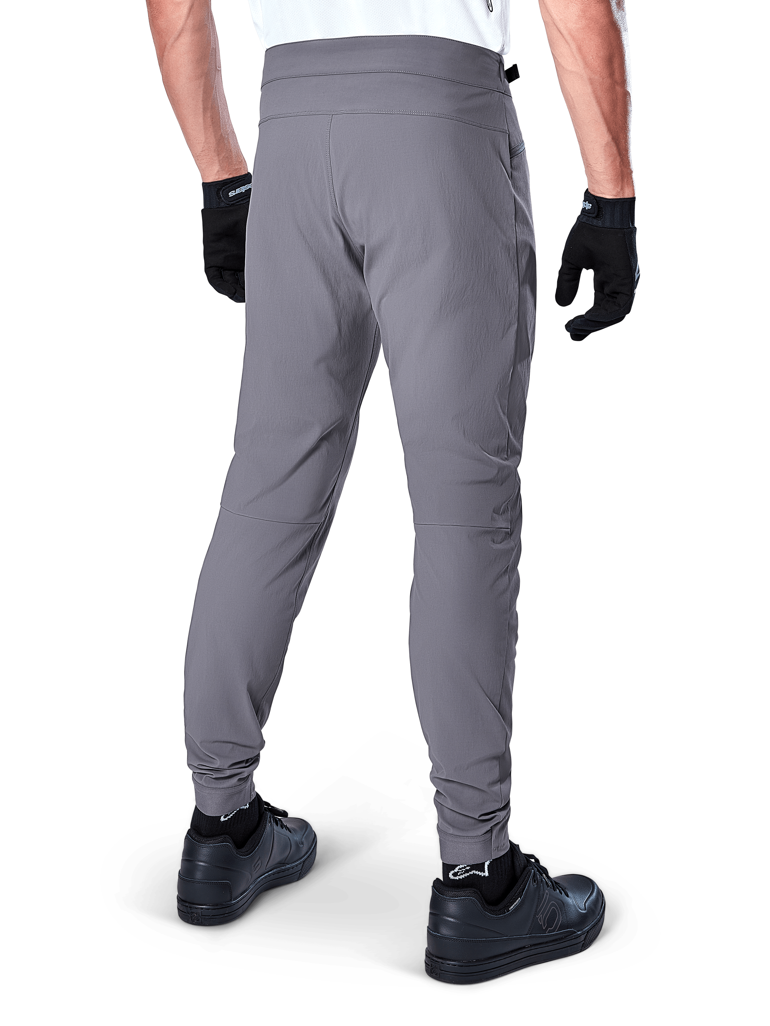 Alpinestars A-Dura Pants, MTB-byxor, mörkgrå, bakvy av modell som bär utrustningen, med ett slitstarkt 2-vägs stretchtyg och elastiska muddar, matchat med svarta handskar och sneakers för en cykelklar look