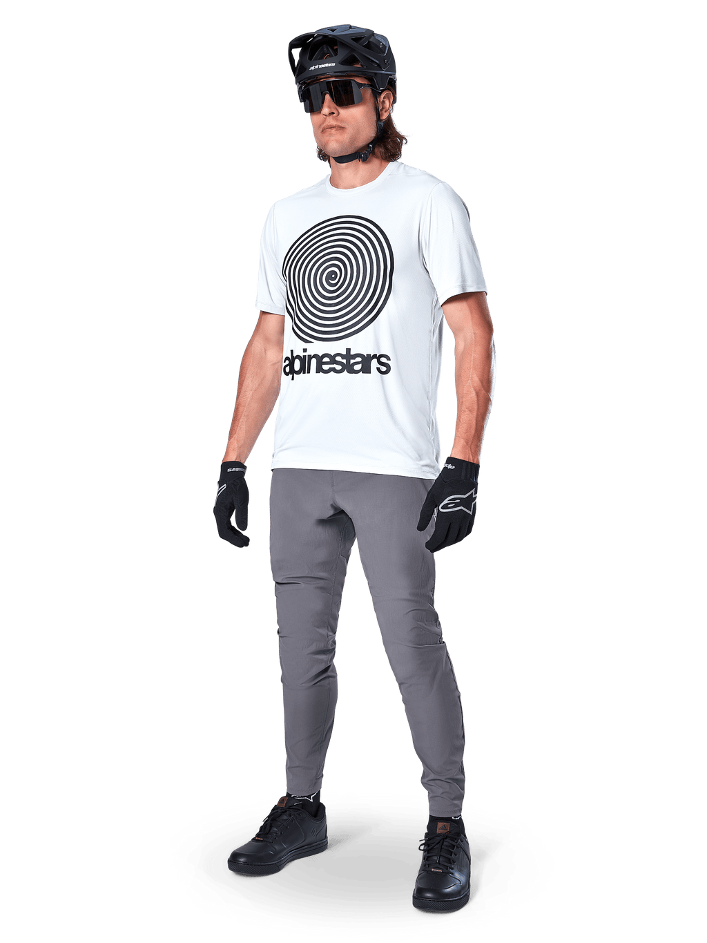 Alpinestars A-Dura Byxor, MTB-byxor, mörkgrå, bärs med vit t-shirt med spiralgrafik, svart MTB-hjälm, solglasögon och svarta handskar, slitstarkt 2-vägs stretchtyg för terrängcykling