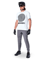Alpinestars A-Dura Byxor, MTB-byxor, mörkgrå, bärs med vit t-shirt med spiralgrafik, svart MTB-hjälm, solglasögon och svarta handskar, slitstarkt 2-vägs stretchtyg för terrängcykling