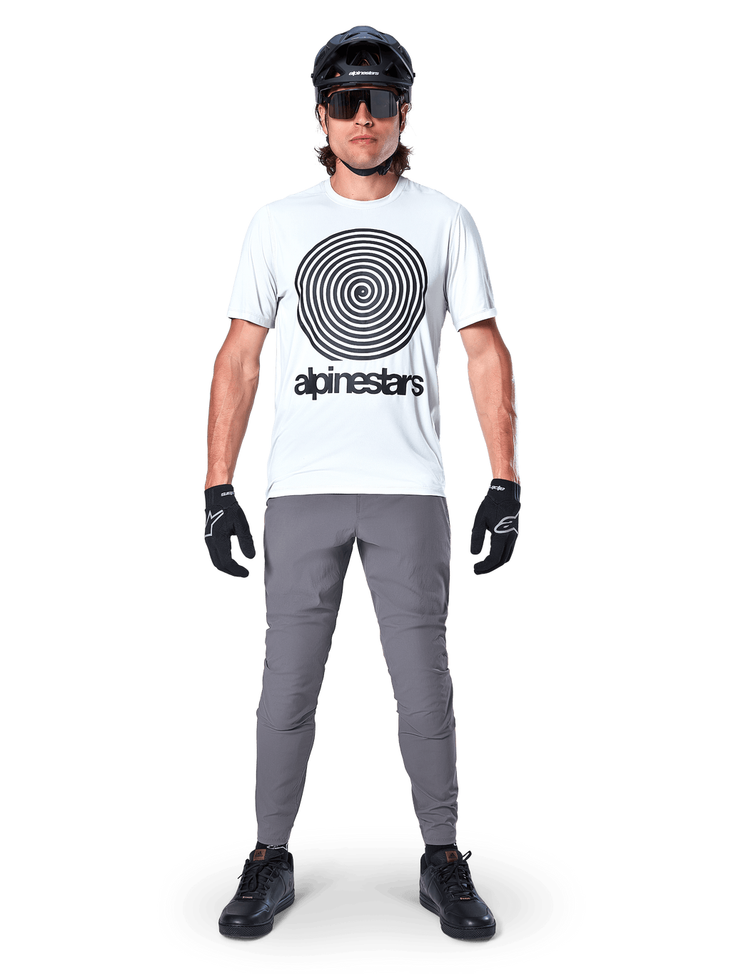 Alpinestars A-Dura byxor, MTB-cykelbyxor, mörkgrå, bärs med en vit grafisk t-shirt, svart hjälm och handskar, med en slitstark 2-vägs stretchdesign och normal passform för mountainbike