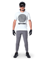 Alpinestars A-Dura byxor, MTB-cykelbyxor, mörkgrå, bärs med en vit grafisk t-shirt, svart hjälm och handskar, med en slitstark 2-vägs stretchdesign och normal passform för mountainbike
