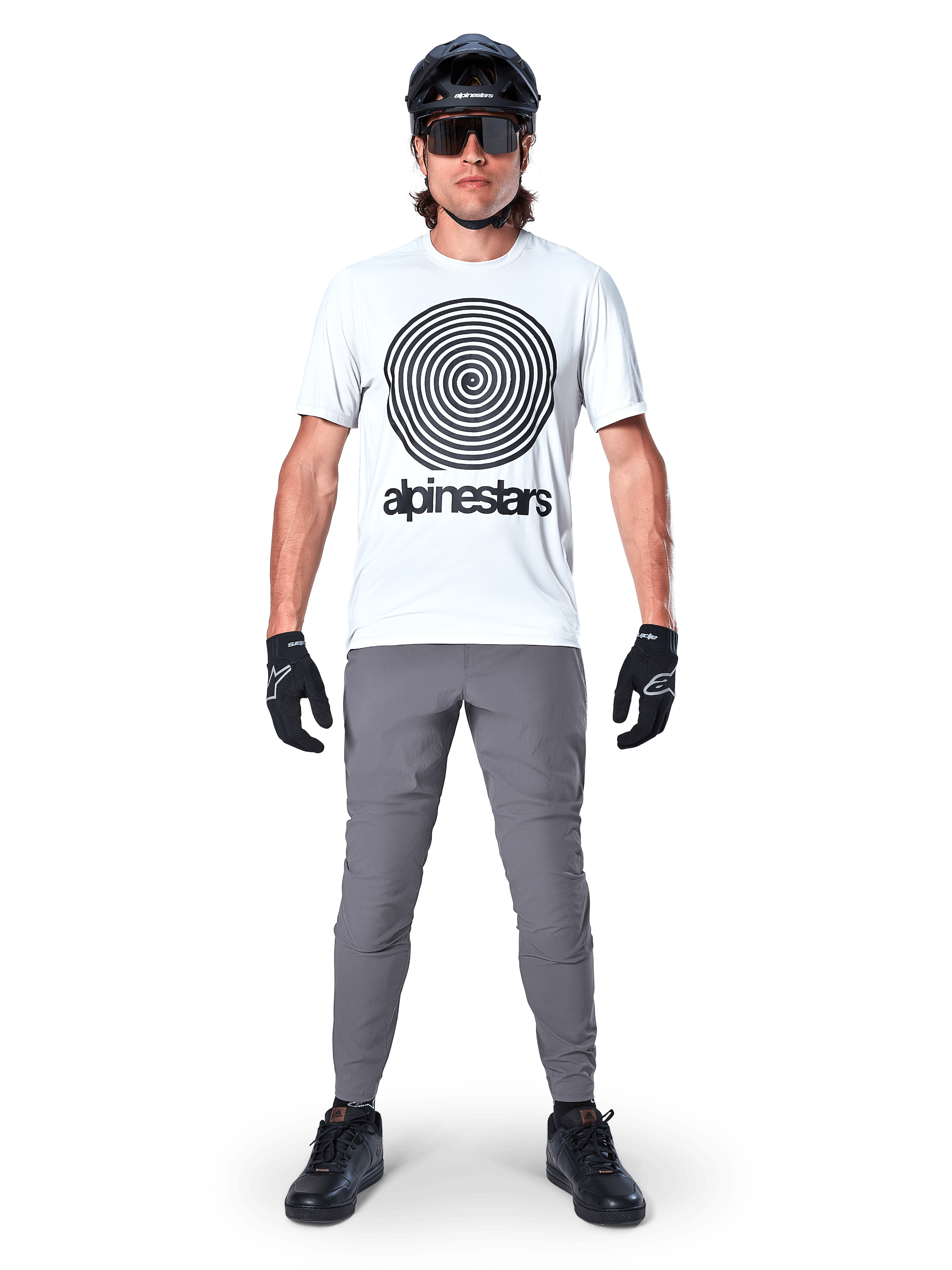 Alpinestars A-Dura byxor, MTB-cykelbyxor, mörkgrå, bärs med en vit grafisk t-shirt, svart hjälm och handskar, med en slitstark 2-vägs stretchdesign och normal passform för mountainbike