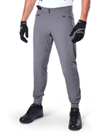 Alpinestars A-Dura Pants, mörkgrå MTB-byxor med dubbel tryckknappsstängning och blixtlåsförsedda fickor, elastiska muddar, bärs med svarta cykelhandskar och svarta sneakers
