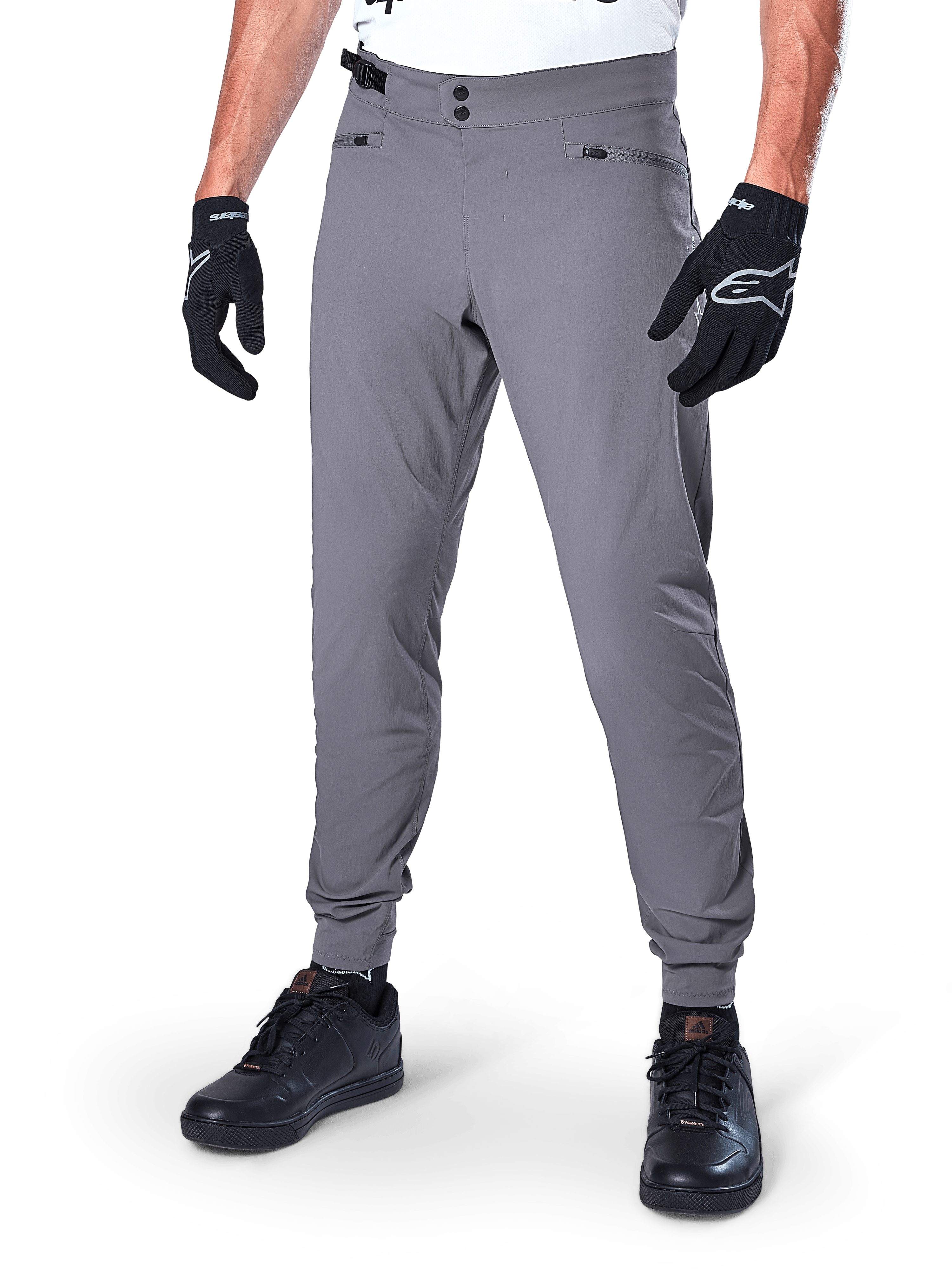 Alpinestars A-Dura Pants, mörkgrå MTB-byxor med dubbel tryckknappsstängning och blixtlåsförsedda fickor, elastiska muddar, bärs med svarta cykelhandskar och svarta sneakers