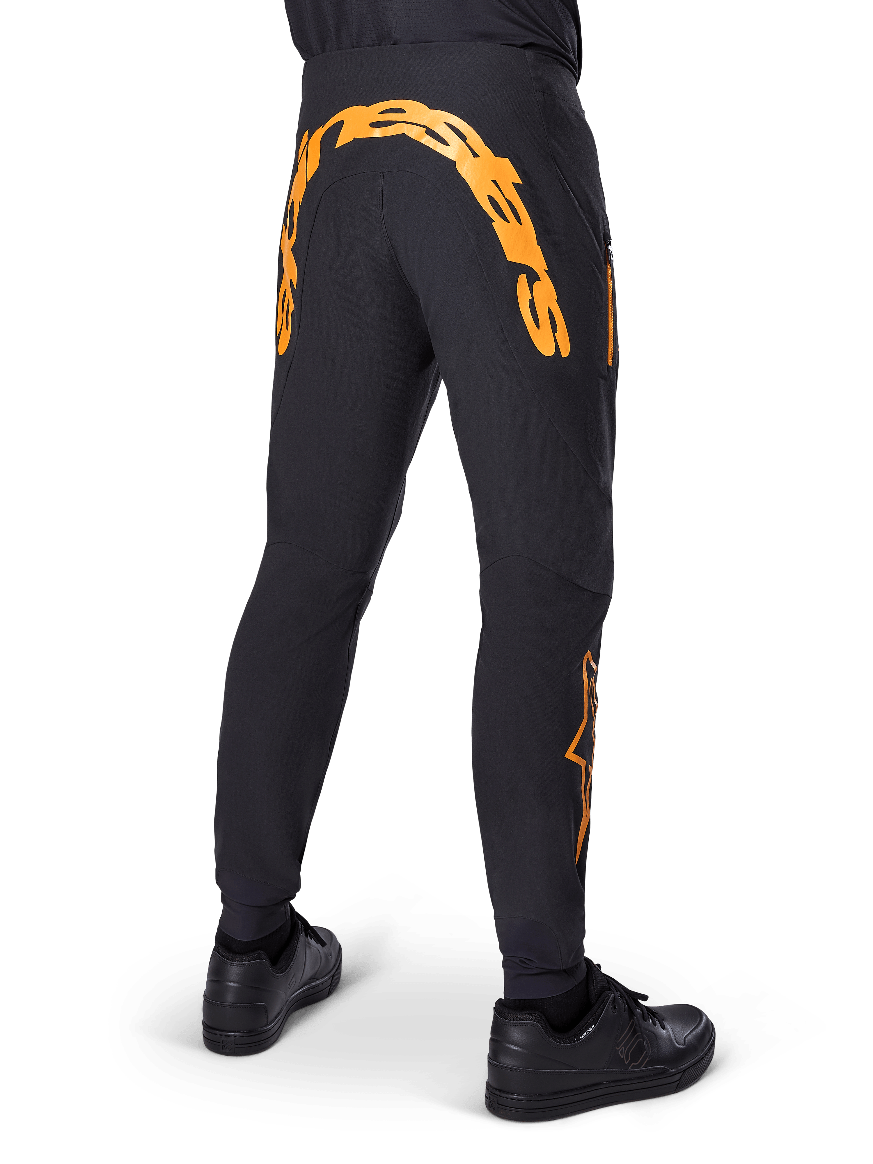 Alpinestars A-Supra Race Pants, Black MTB Pants, Rear view featuring large orange Alpinestars wordmark across the back yoke, orange logo on the lower leg, performance fit with zippered pocket, worn with black shoes
