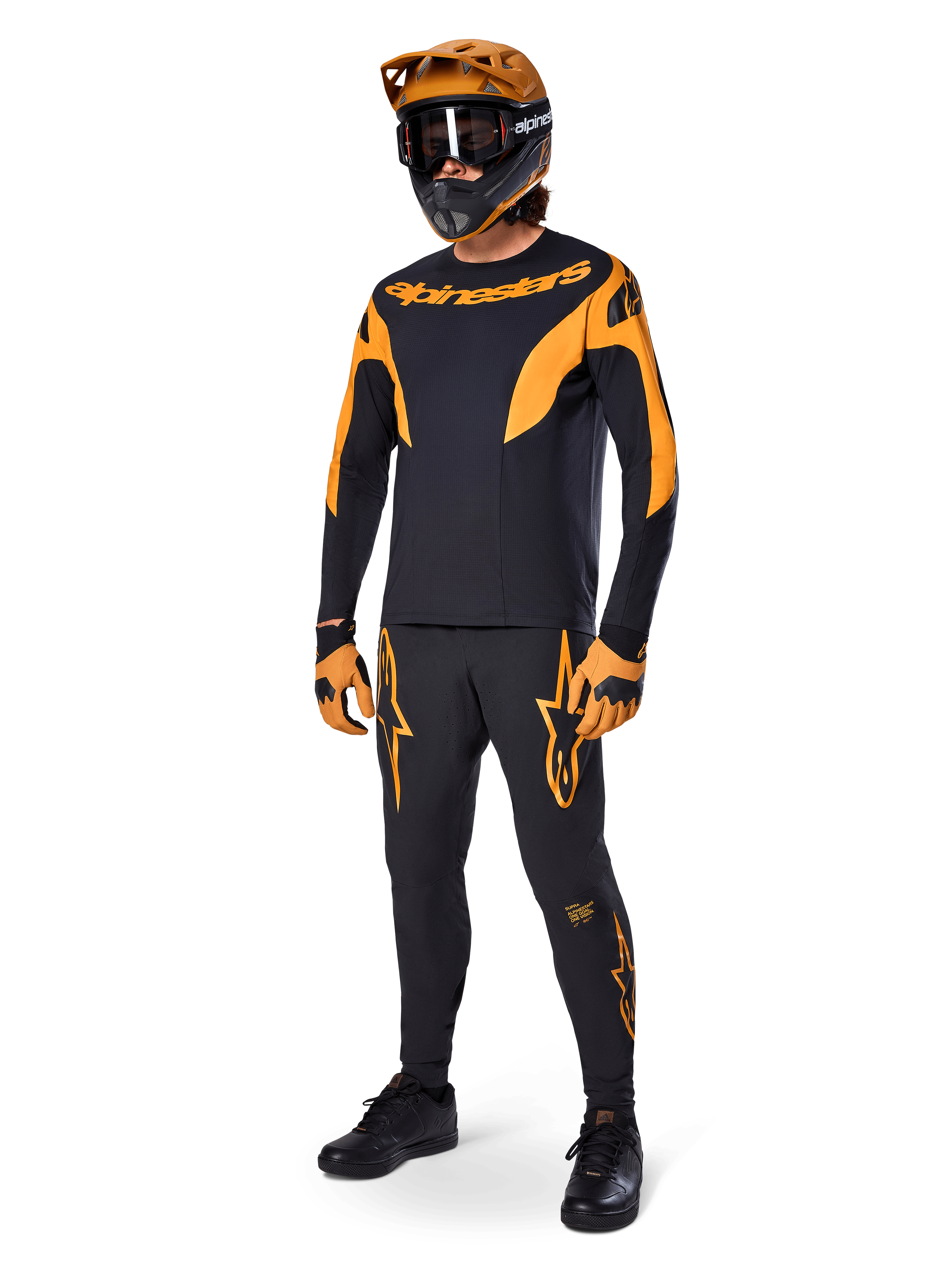 Mountain bike rider wearing complete racing gear, Alpinestars A-Supra Race Pants in black with orange accents, matching black and orange long-sleeve jersey, orange helmet with black goggles, orange and black gloves, and black shoes, professional MTB racing kit design