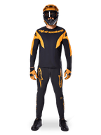 Alpinestars A-Supra Race Pants, MTB Racing Pants, Black and Orange, worn by a rider in a complete racing kit including a black and orange jersey, orange helmet, and matching gloves, featuring bold orange star logos on the legs