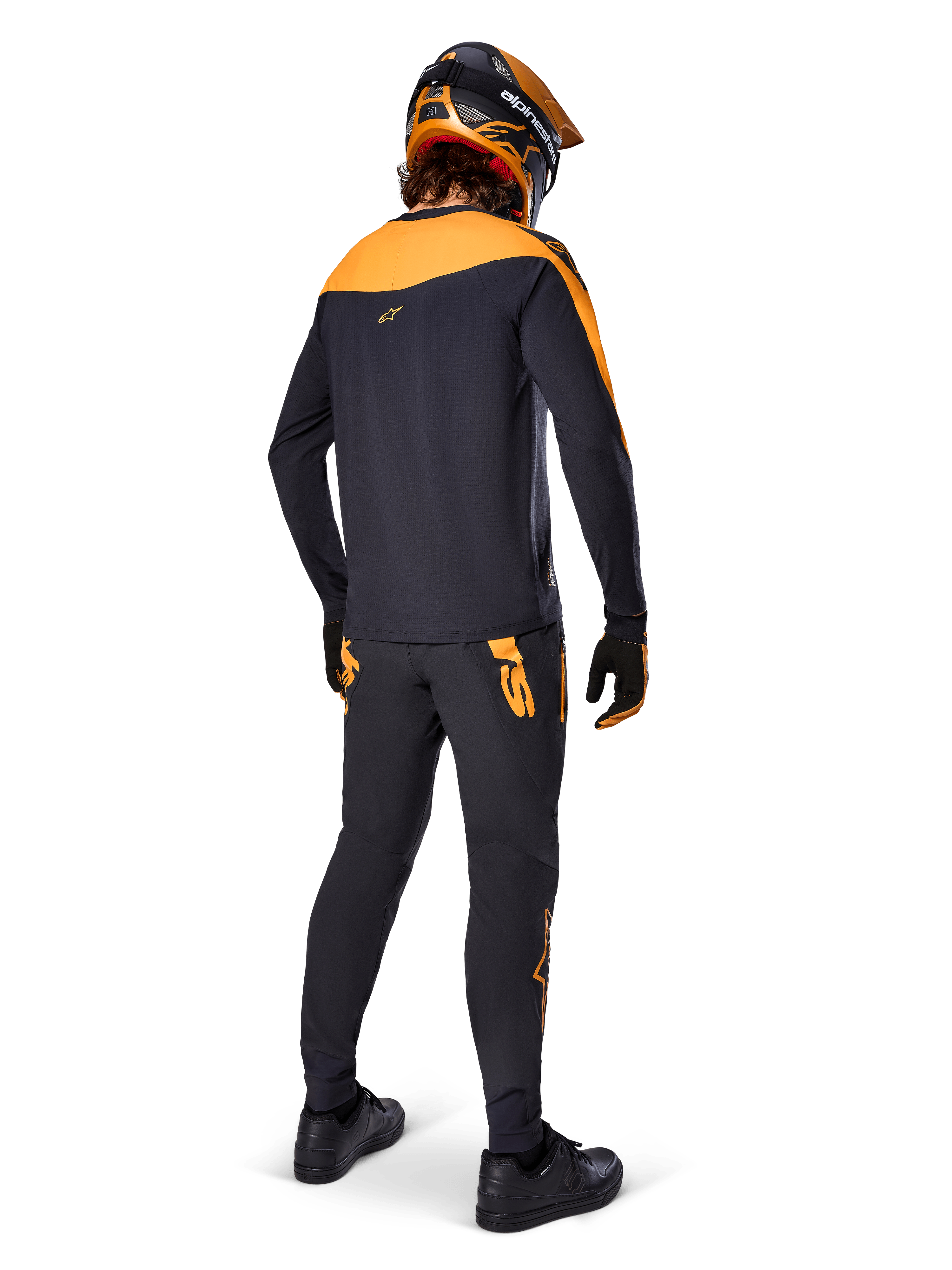 Alpinestars A-Supra Race Pants, MTB Racing Pants, Black with orange logos, viewed from the back on a rider wearing a matching black and orange jersey, helmet, and gloves, highlighting the MX-inspired wordmark on the back yoke and performance fit for technical trails.