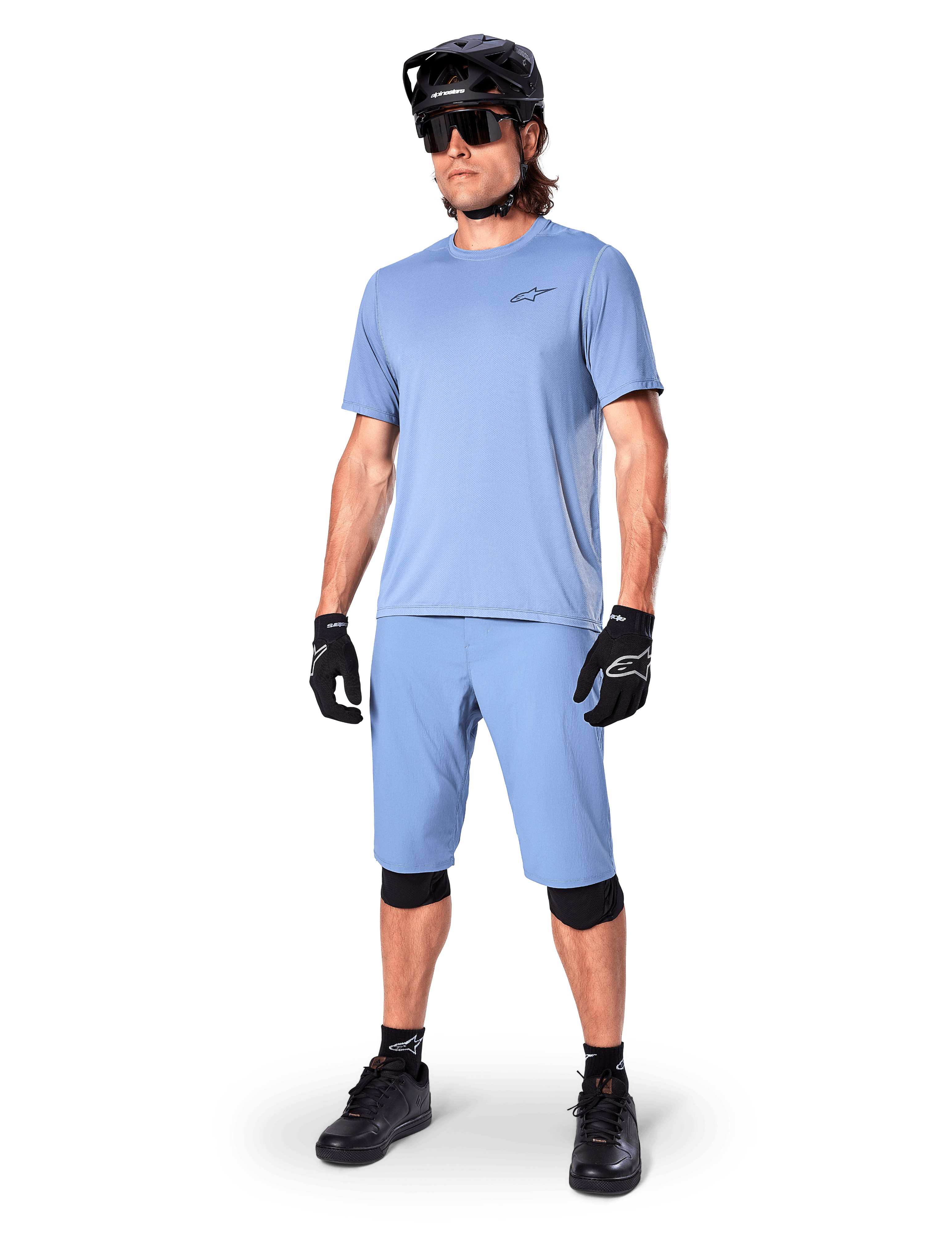 Modell klädd i Alpinestars A-Dura Shorts i Infinity Blue, matchande ljusblå kortärmad tröja, svart MTB-hjälm, solglasögon och svarta handskar, komplett mountainbike-outfit för stigcykling